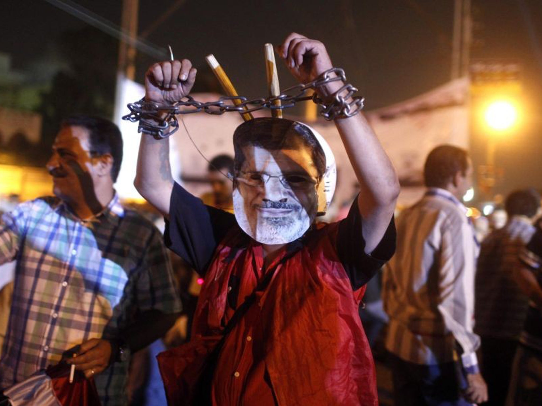 An anti-Morsi protester wears a mask depicting deposed president, and chains on his hands, close to the presidential palace in Cairo