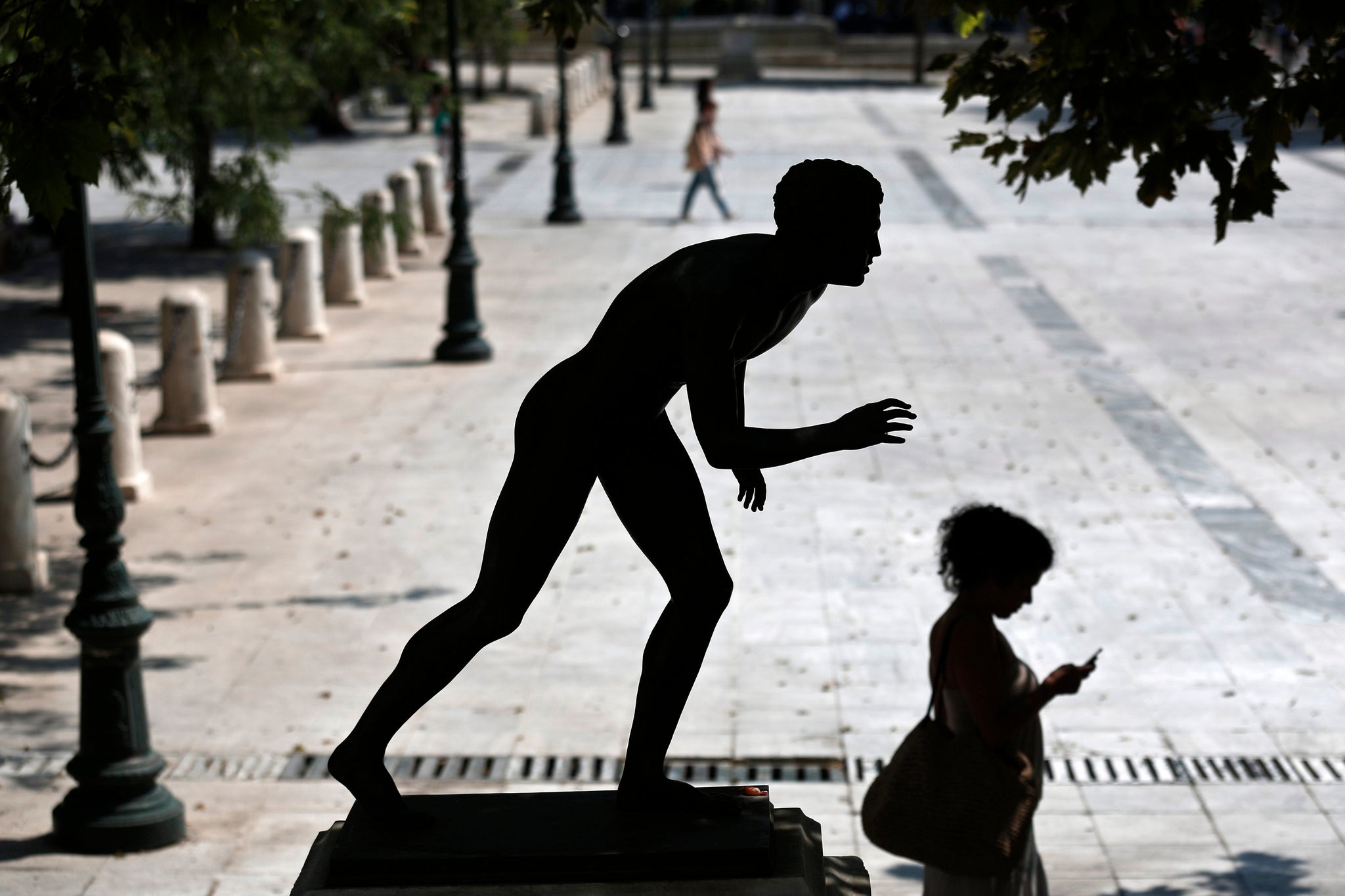 A woman checks her mobile phone as she walks past a statue at central Syntagma square in Athens July 3, 2013. REUTERS/Yorgos Karahalis