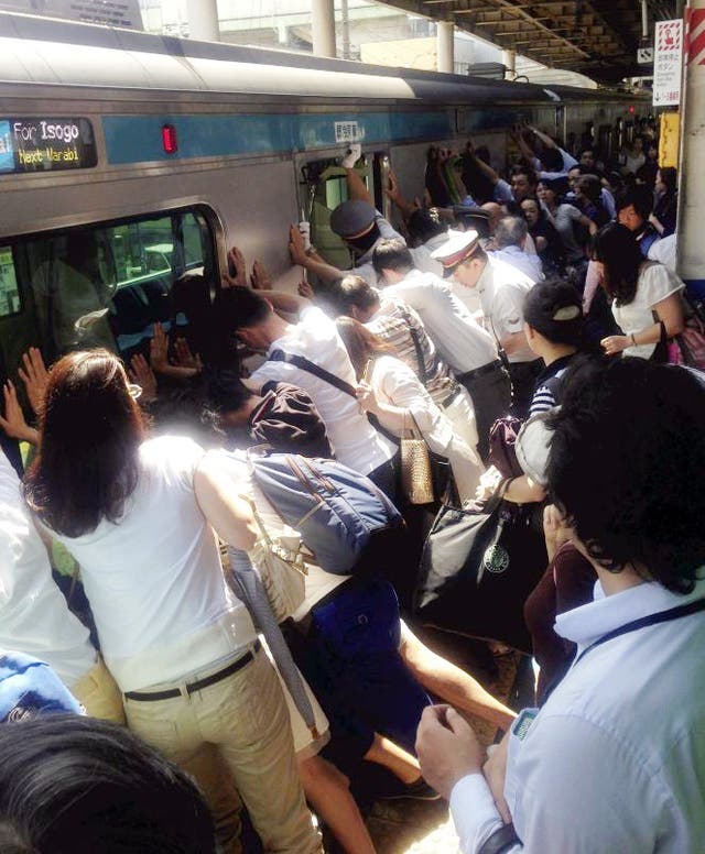 Train passengers and railway staff push a train car in their effort to rescue a woman who fell and got stuck between the car and the platform while getting off at Japan Railway Minami Urawa Station in Saitama, near Tokyo