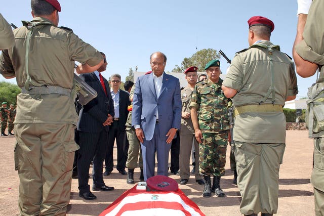 President Moncef Marzouki stands in front of coffin, draped in the Tunisian flag, of the one of the eight soldiers who died in an ambush by an armed group in Mount Chaambi