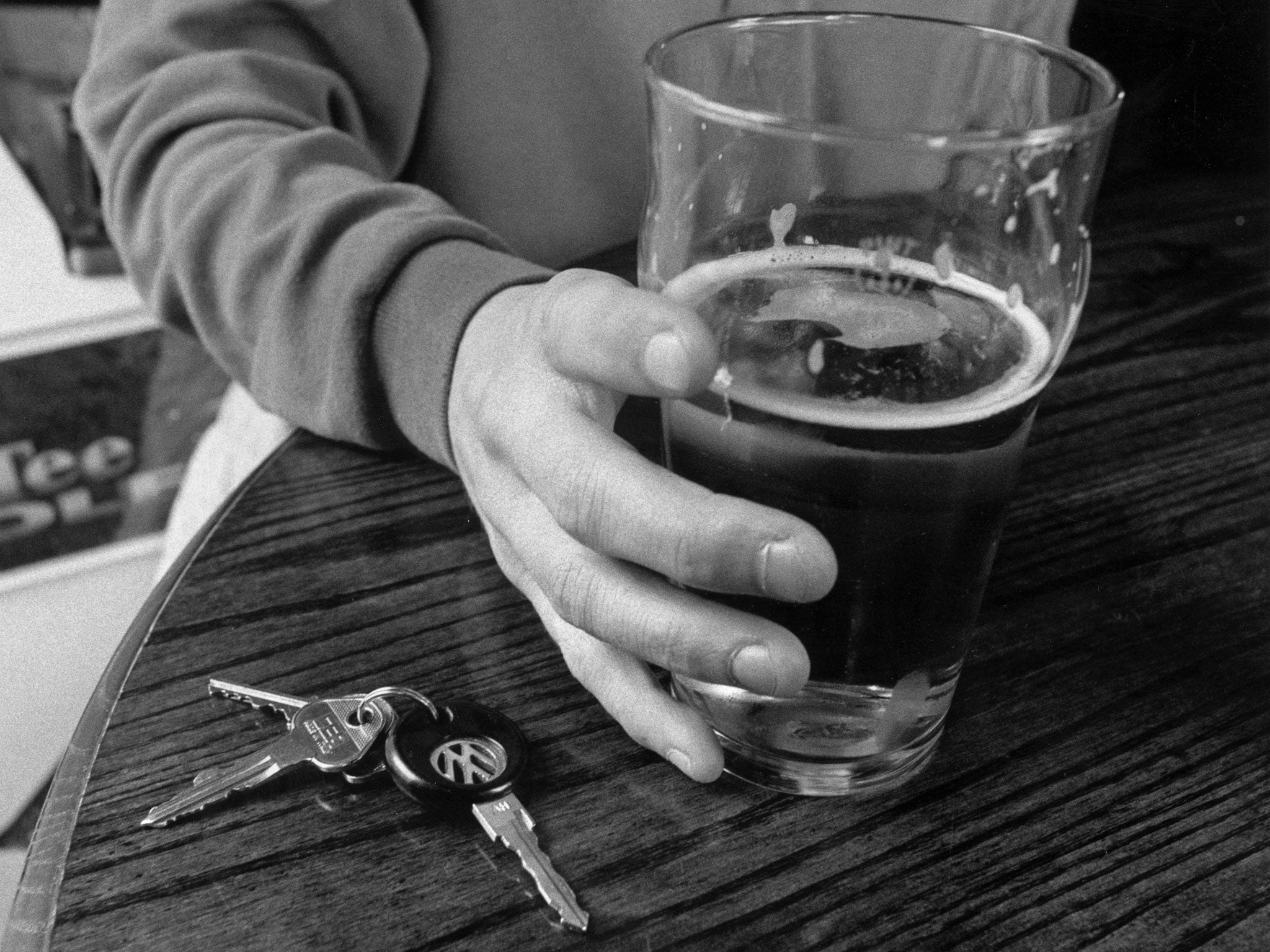 A man holding a pint of lager with his car keys next to it on a table in a British pub, 3rd July 1997.