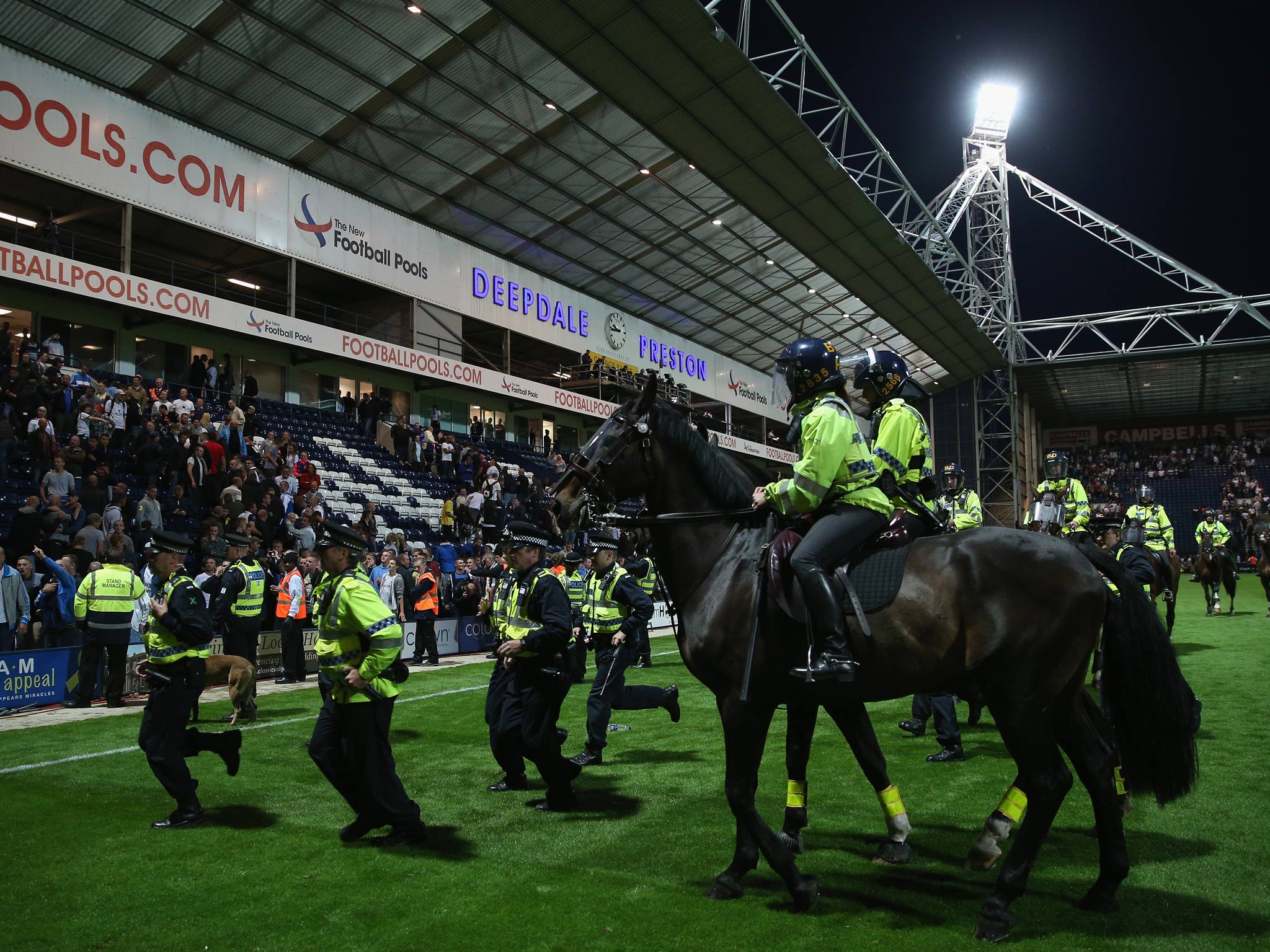 Police on foot and horse try to control the pitch invasion by fans at the final whistle of the Capital One Cup first round match between Preston North End and Blackpool
