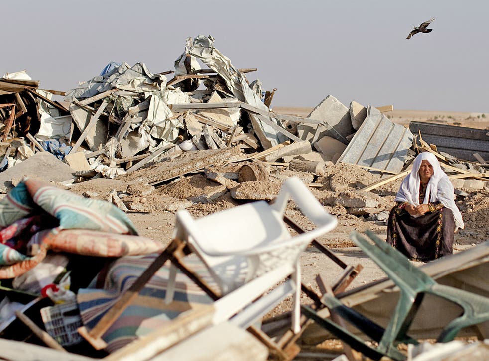 A Bedouin woman sits next to what is left of houses destroyed by Israeli authorities in Al-Akarib village, in the Israeli Negev Desert