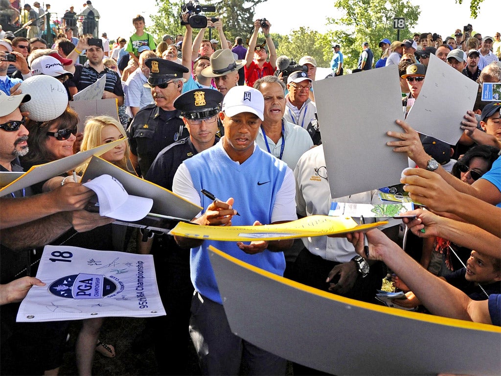 Tiger Woods signs autographs while walking off the 18th green following Tuesday's practice session