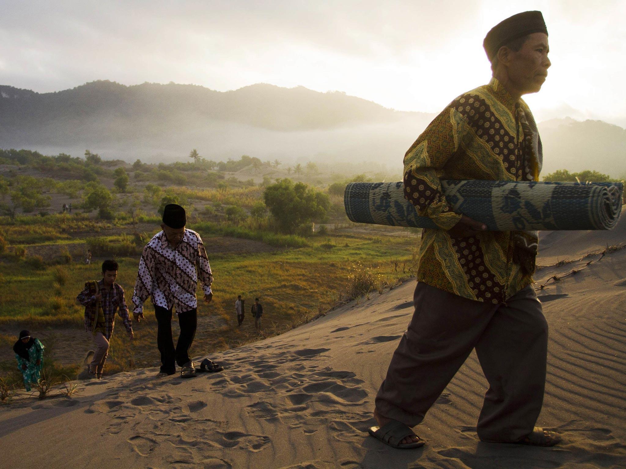 People walk through sand to attend Eid al-Fitr prayers at Parang Kusumo beach
