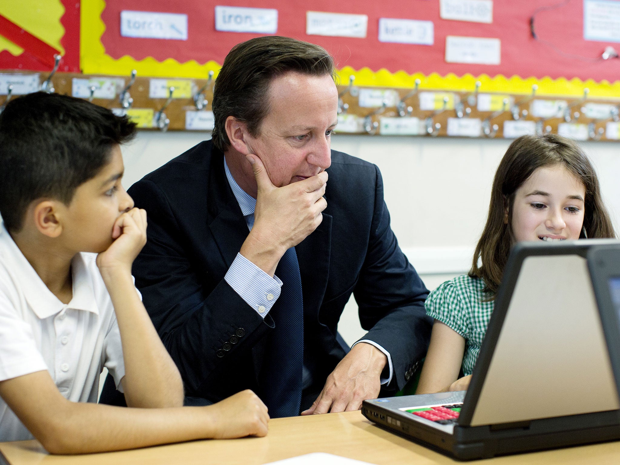 Britain's Prime Minister David Cameron sits with pupils Abdullah Rashid (9) and Anna Seitoar (9) in a computer class during his visit to St Mary's and St John's CE School in north London on July 8, 2013.