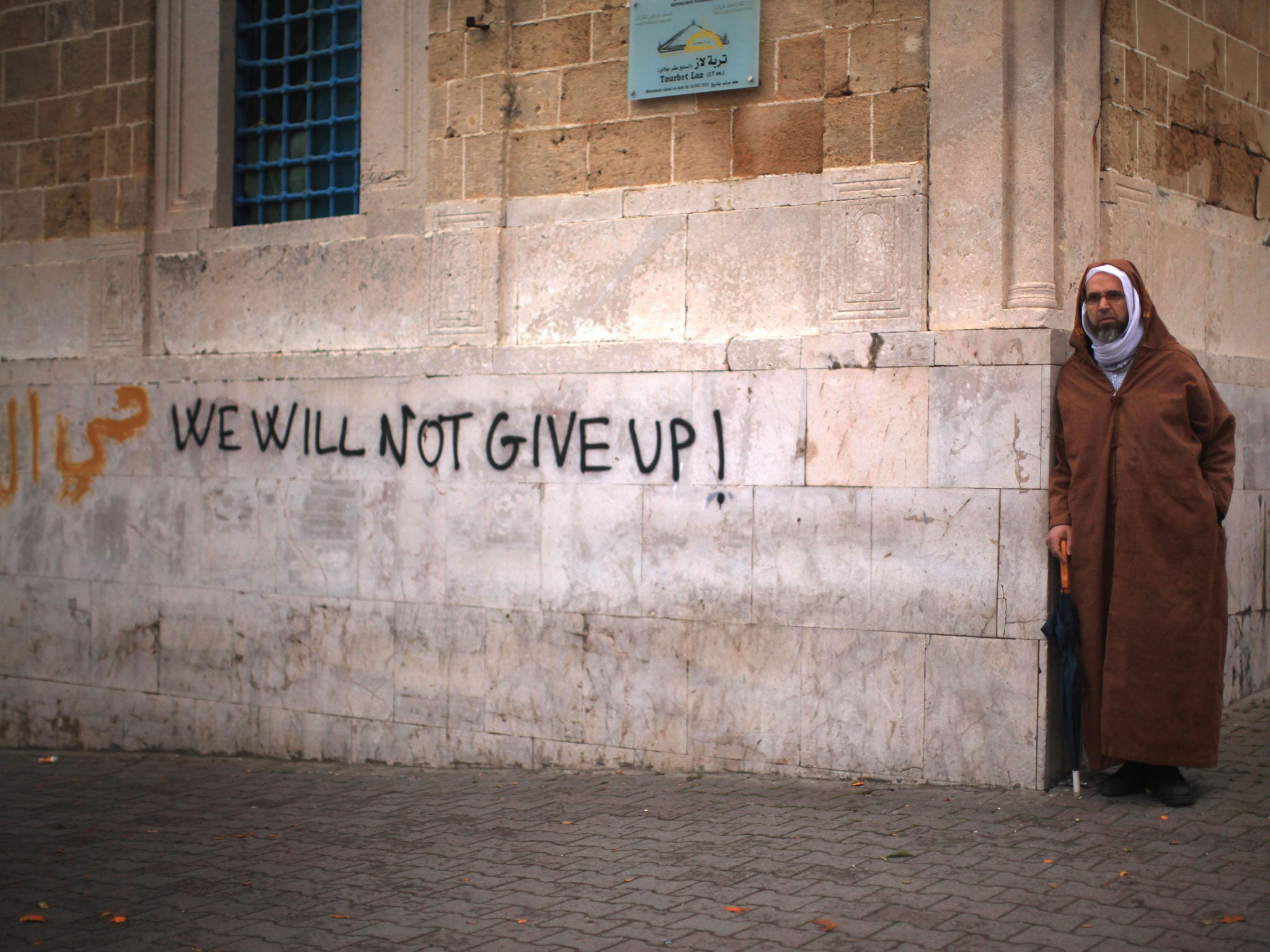 A Tunisian man looks on next to graffiti as protestors continue their demonstrations outside Prime Minister Mohammed Ghannouchi's offices in Government Square Tunis on January 25, 2011 in Tunis, Tunisia.