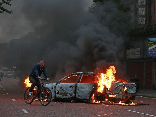 A man cycles past a burning car after Loyalist protesters attacked the police with bricks and bottles