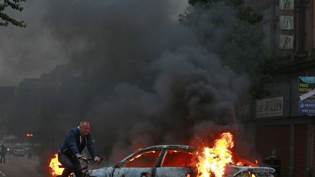 A man cycles past a burning car after Loyalist protesters attacked the police with bricks and bottles