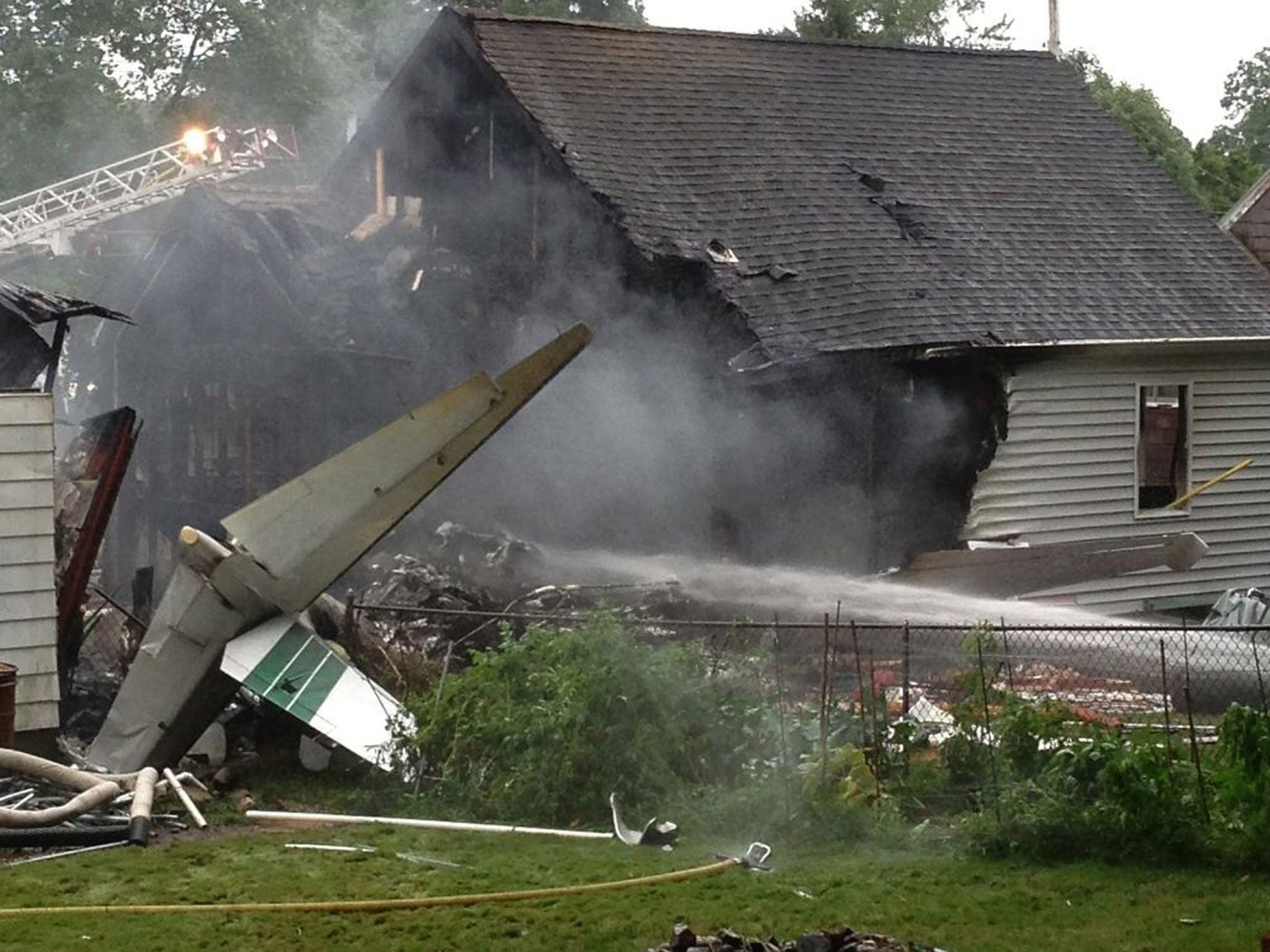The tail of a small aircraft sits behind a burned home following a crash in East Haven, Connecticut