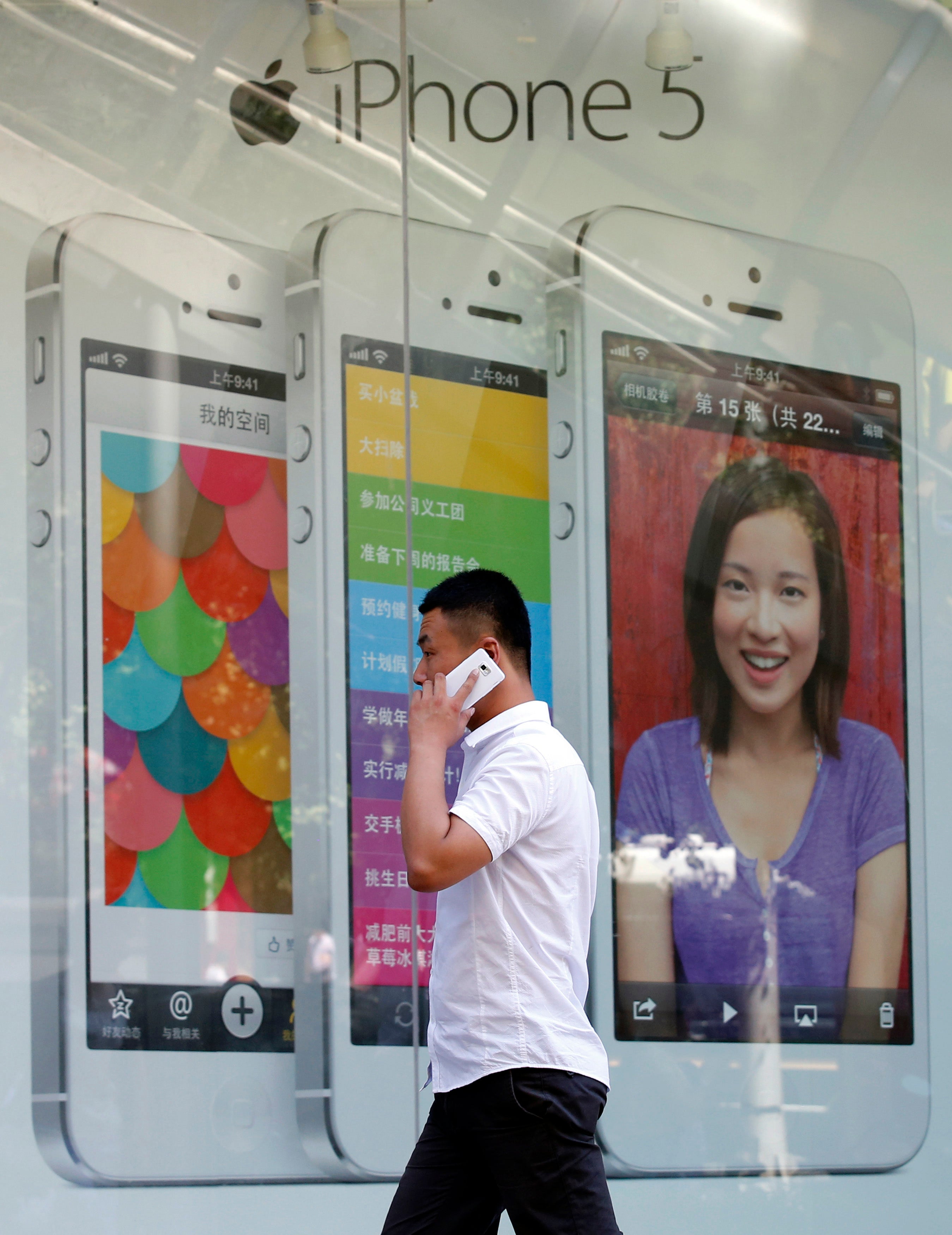 A man talks on a mobile phone as he walks past an iPhone advertising board in Beijing July 24, 2013. REUTERS/Kim Kyung-Hoon