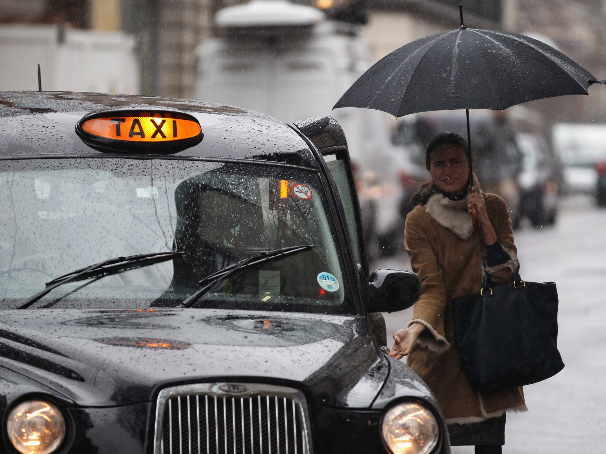 A woman holding an umbrella catches a London taxi in the pouring rain