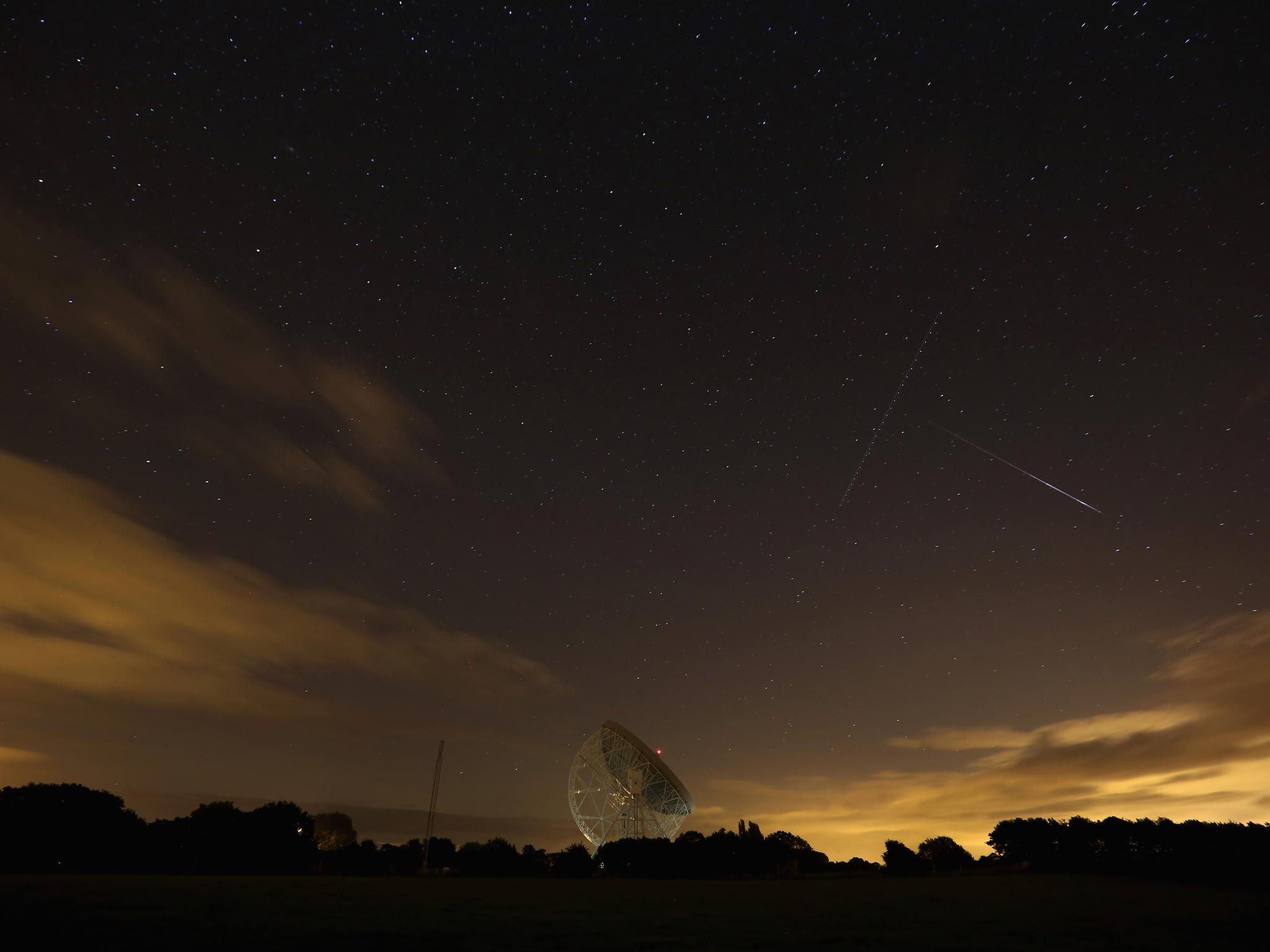 A Perseid meteor (right) streaks across the sky past the light trail of an aircraft over the Lovell Radio Telescope at Jodrell Bank in Holmes Chapel, United Kingdom