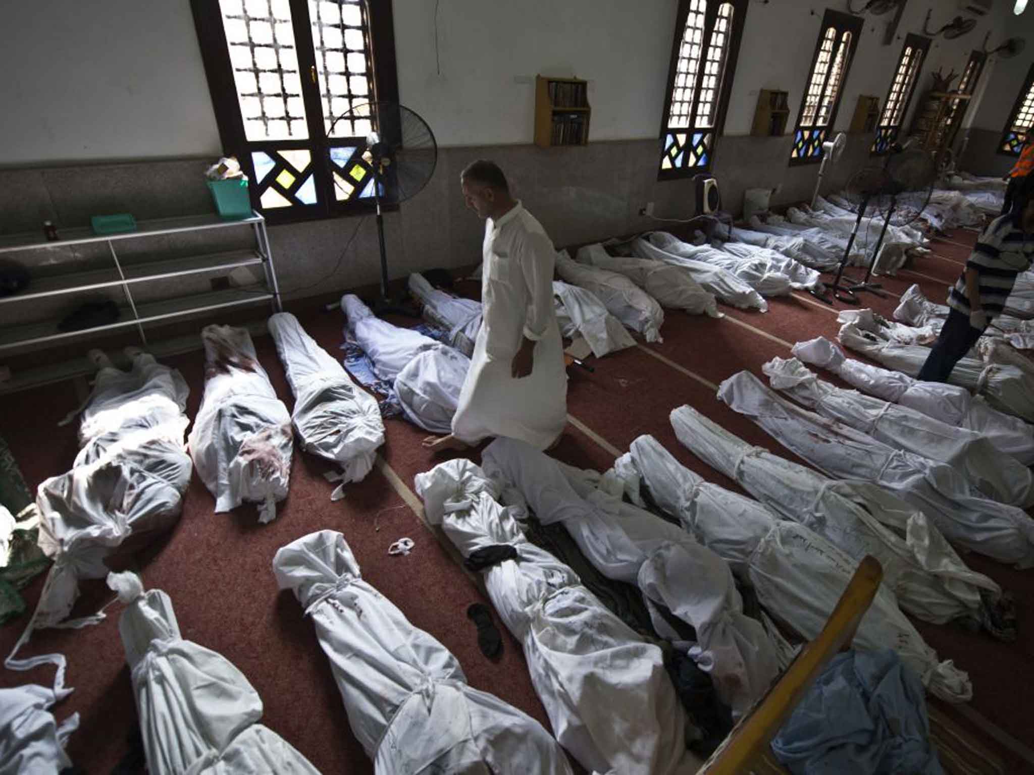 An Egyptian man walks between lines of bodies wrapped in shrouds. The day's violence was Egypt's worst in decades
