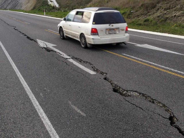 A car drives past a crack in a road after an earthquake on the outskirts of the town of Seddon