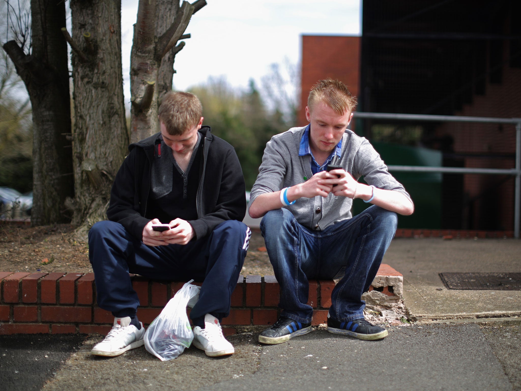 Two youths send text messages on their smart phones in Corby, Northamptonshire, the youth unemployment capital of Britain, on April 24, 2013 in Corby, England.