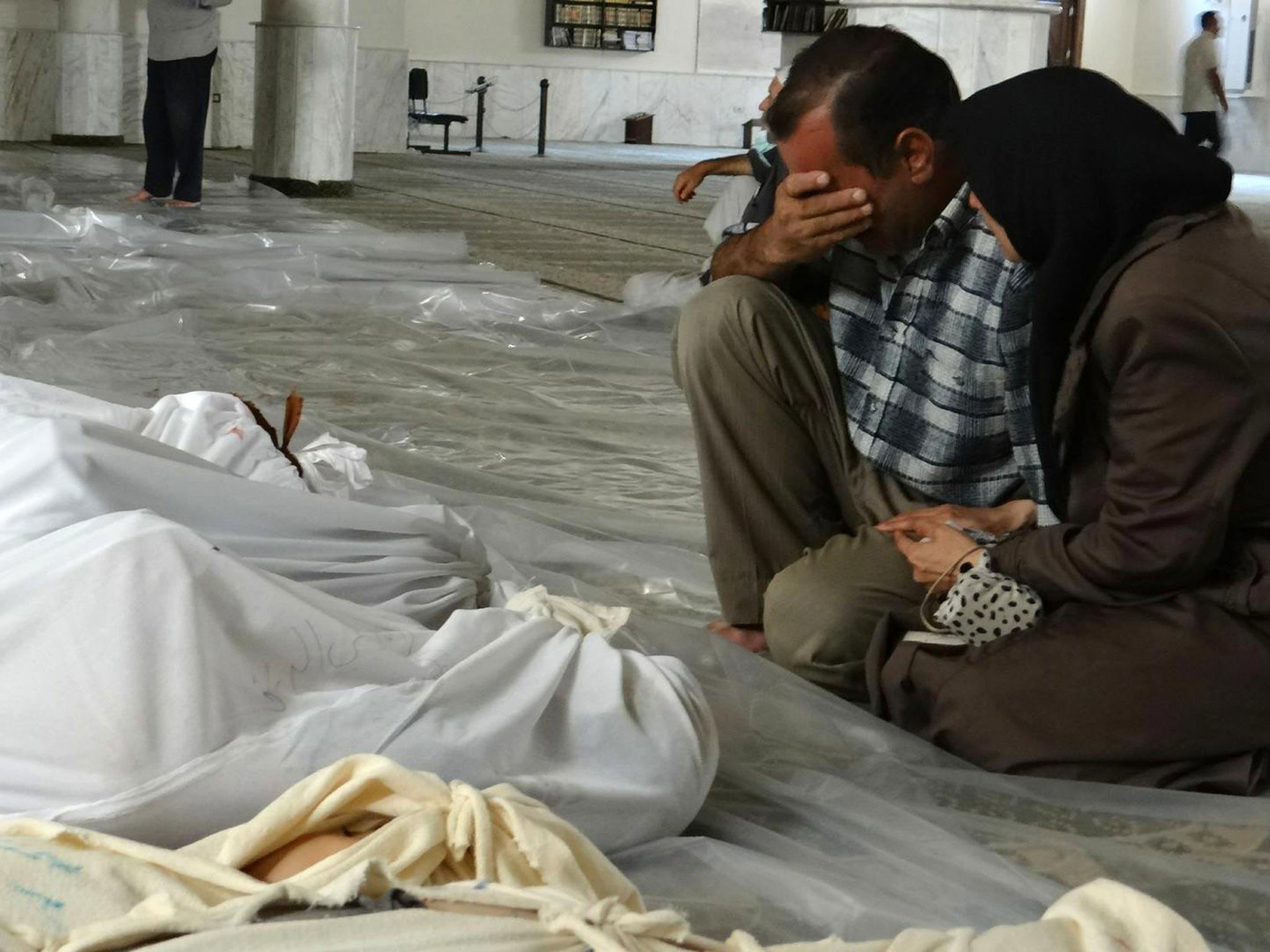 A Syrian couple mourning in front of bodies wrapped in shrouds ahead of funerals following what Syrian rebels claim to be a toxic gas attack by pro-government forces in eastern Ghouta, on the outskirts of Damascus
