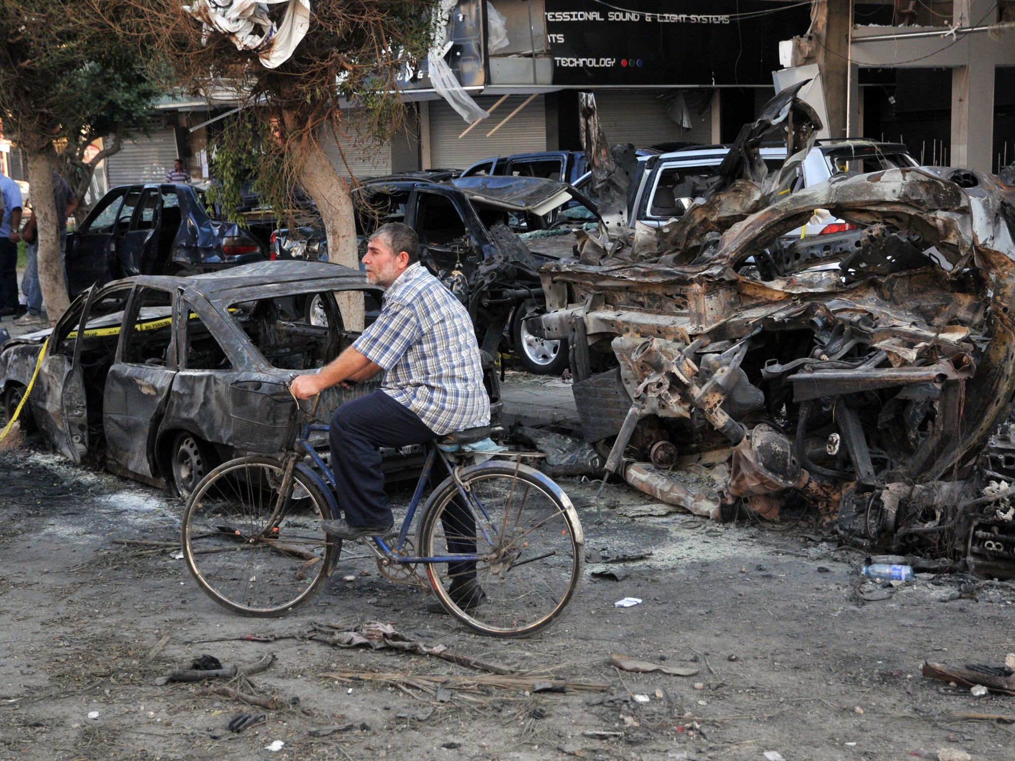 A Lebanese drives his bicycle past burnt vehicles at the site of one of the two explosions that struck the northern city of Tripoli