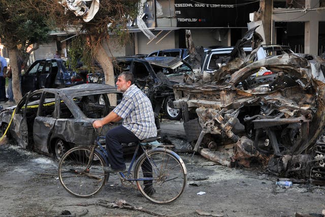 A Lebanese drives his bicycle past burnt vehicles at the site of one of the two explosions that struck the northern city of Tripoli 