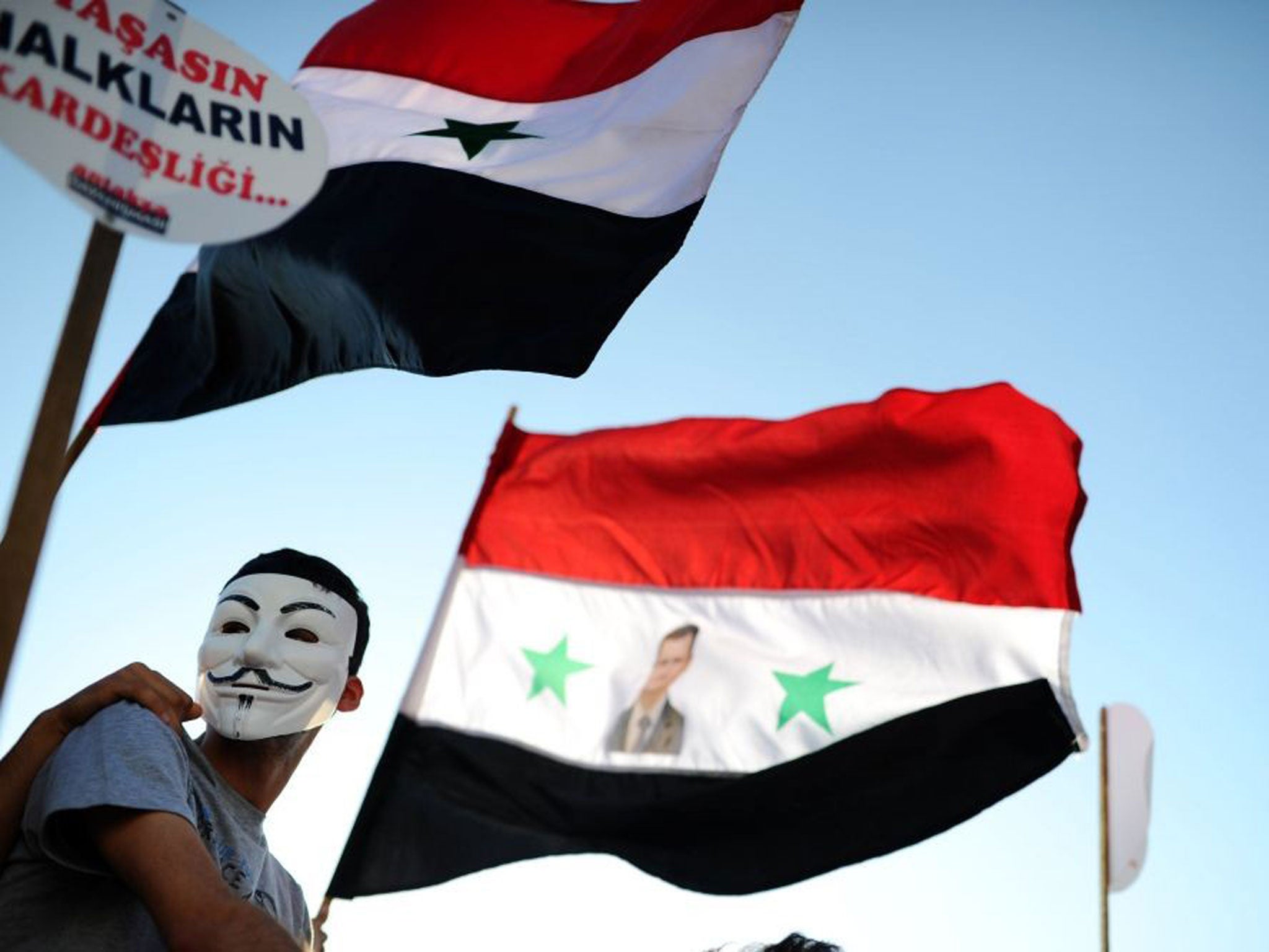 A protester waves a Syrian flag with the photograph of Syrian President Bashar al-Assad, during a rally against a possible attack on Syria in the bordering Turkish province of Hatay, 1 September