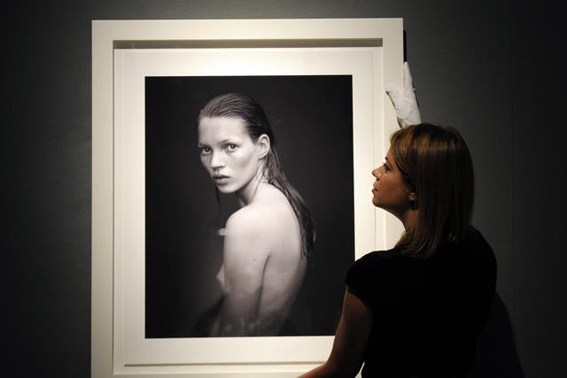 A gallery employee places a photograph of Kate Moss taken for Calvin Klein Obsession campaign in 1993 by US photographer Mario Sorrenti, during a press view of an auction of a selection of works featuring her at Christie's auction house in London