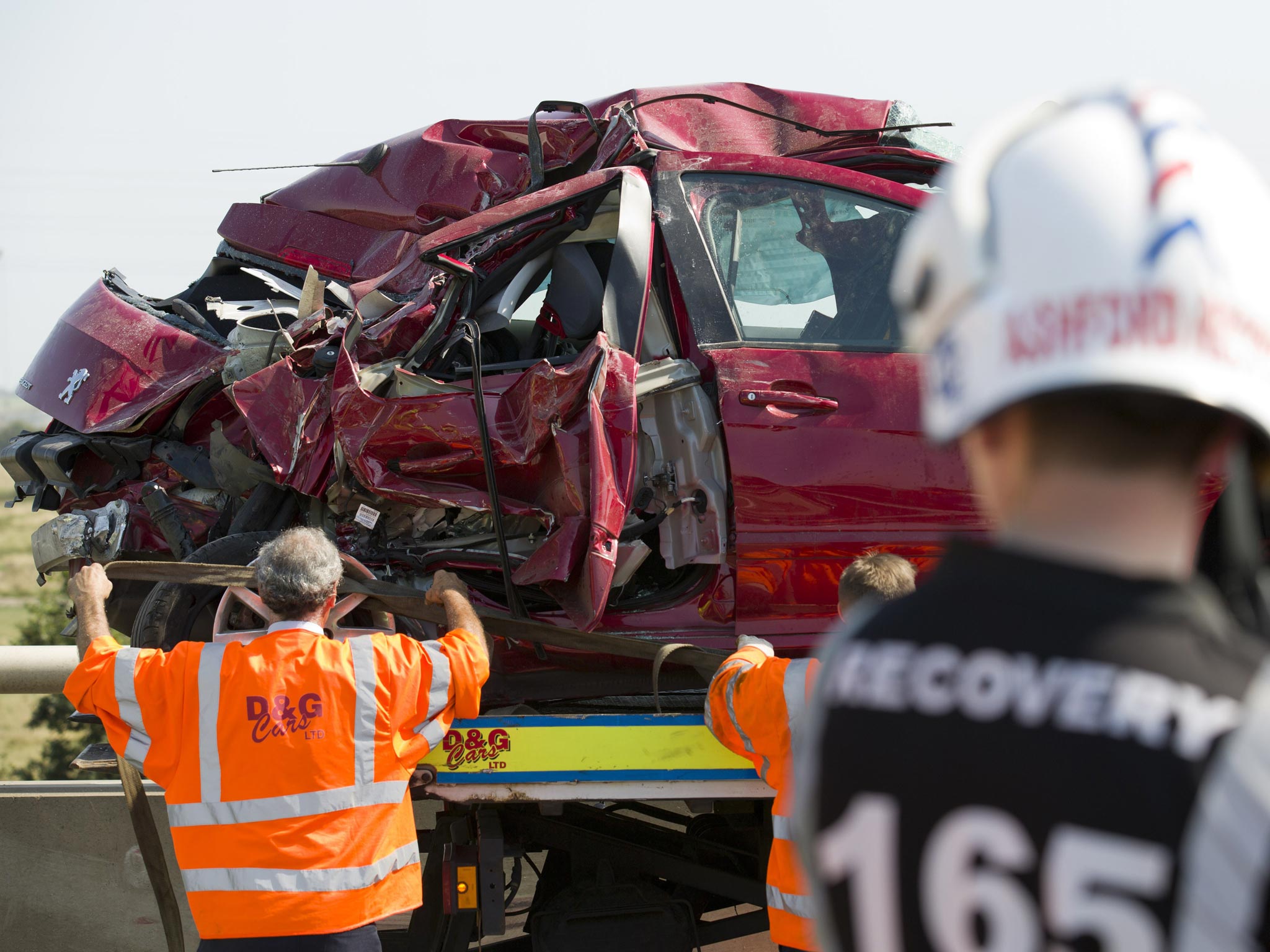 A recovery worker straps the wreckage of a vehicle onto a tow truck