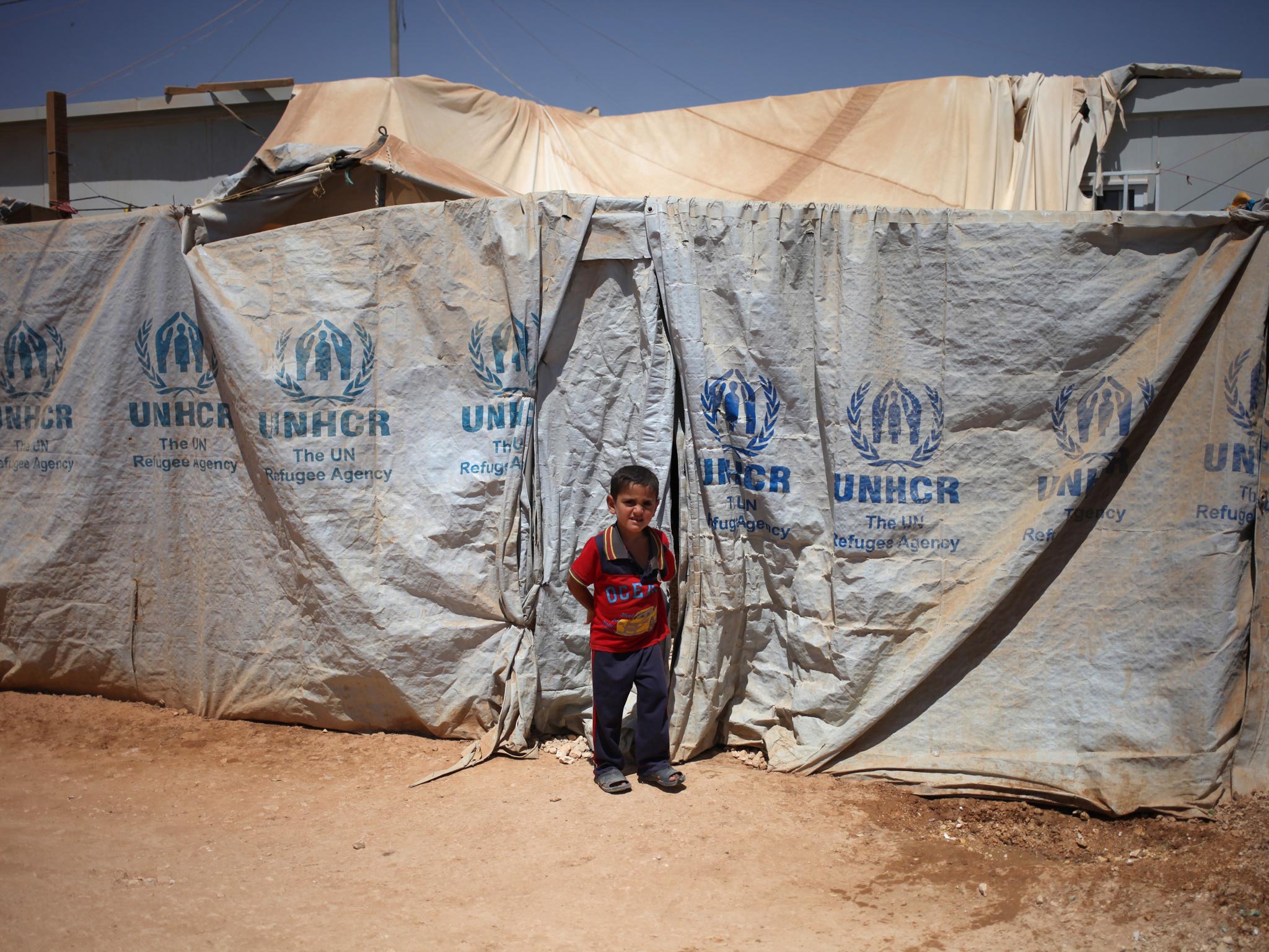 &#13;
A Syrian refugee boy stands in front of his family's makeshift home at Zaatari refugee camp. David Cameron has promised to accept 20,000 Syrians from camps &#13;