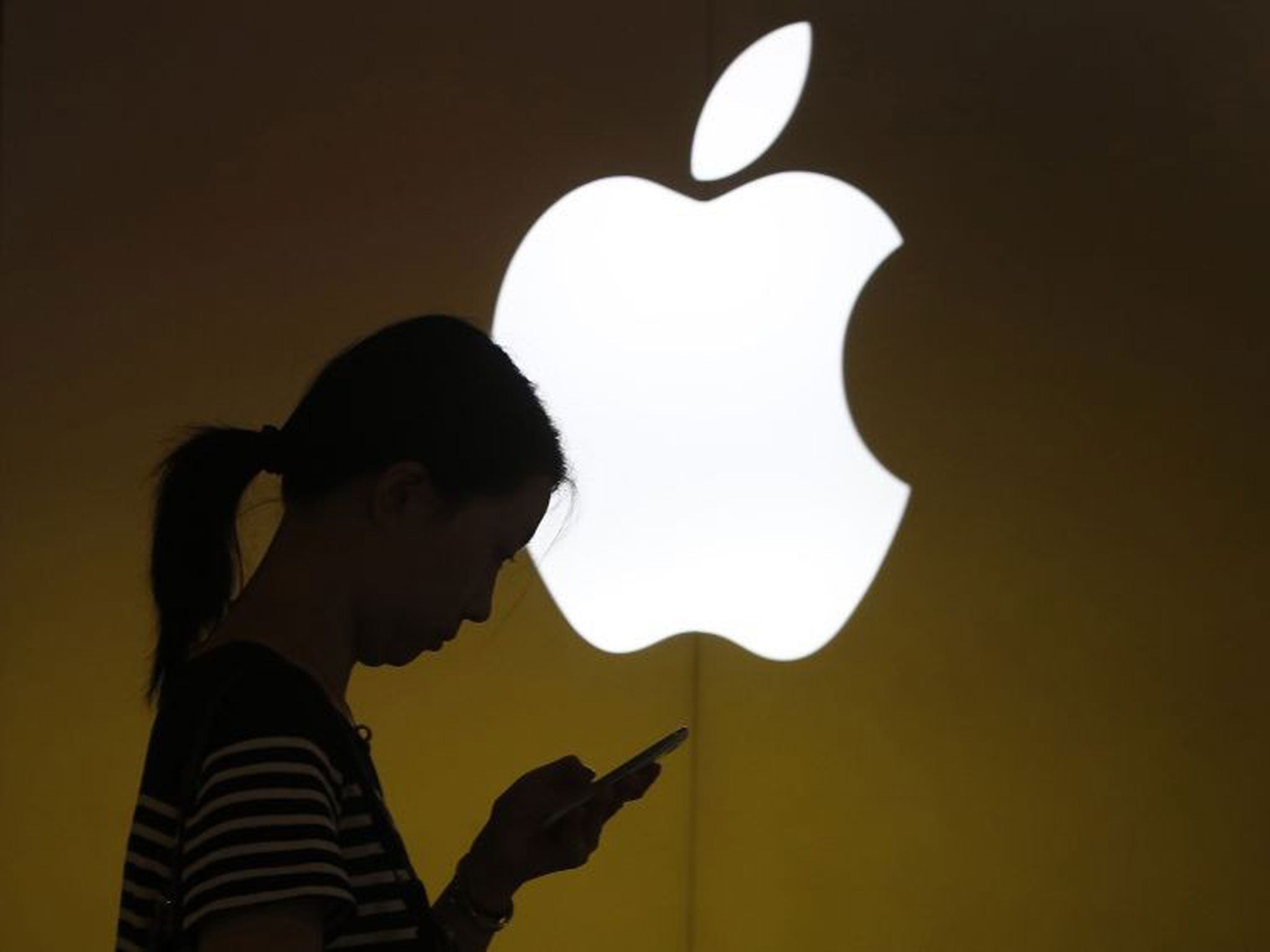 A woman looks at the screen of her mobile phone in front of an Apple logo outside its store in downtown Shanghai September 10, 2013