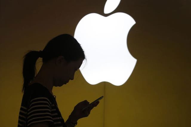 A woman looks at the screen of her mobile phone in front of an Apple logo outside its store in downtown Shanghai September 10, 2013. Apple Inc is expected to introduce a cheaper version of the iPhone on Tuesday, bringing one of the industry's costliest smartphones within reach of the masses in poorer emerging markets