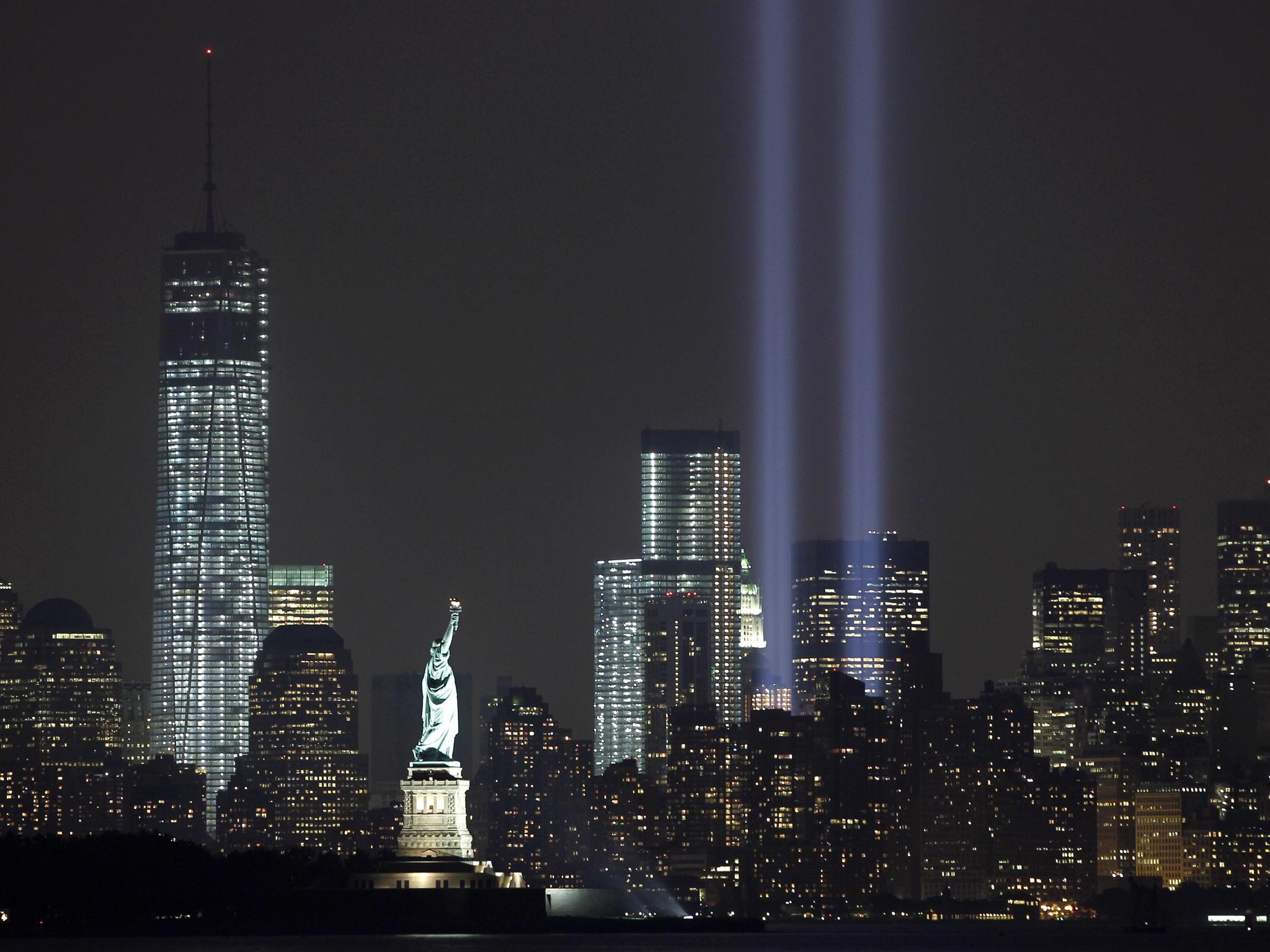 The Tribute in Light is illuminated next to the Statue of Liberty (C) and One World Trade Center (L) during events marking the 12th anniversary of the 9/11 attacks on the World Trade Center in New York