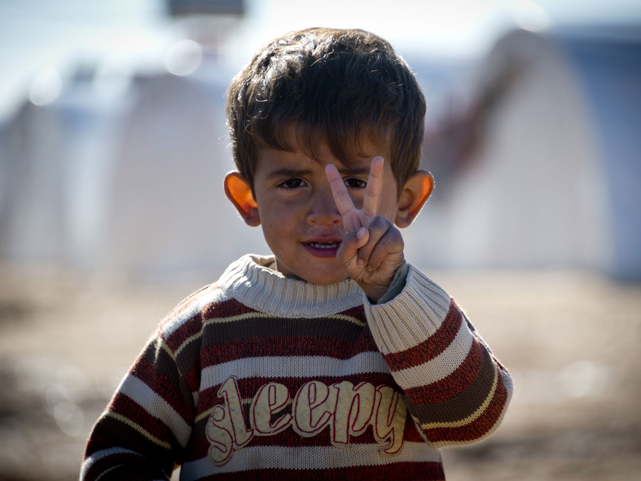 Standing in front of a row of plastic tents a young boy flashes the V-sign in a refugee camp on the border between Syria and Turkey near the northern city of Azaz