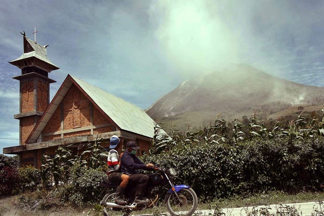 Indonesian villagers ride a motorbike as Mount Sinabung spews hot gas and ashes in the background during an eruption in Karo, North Sumatra province,  Indonesia 