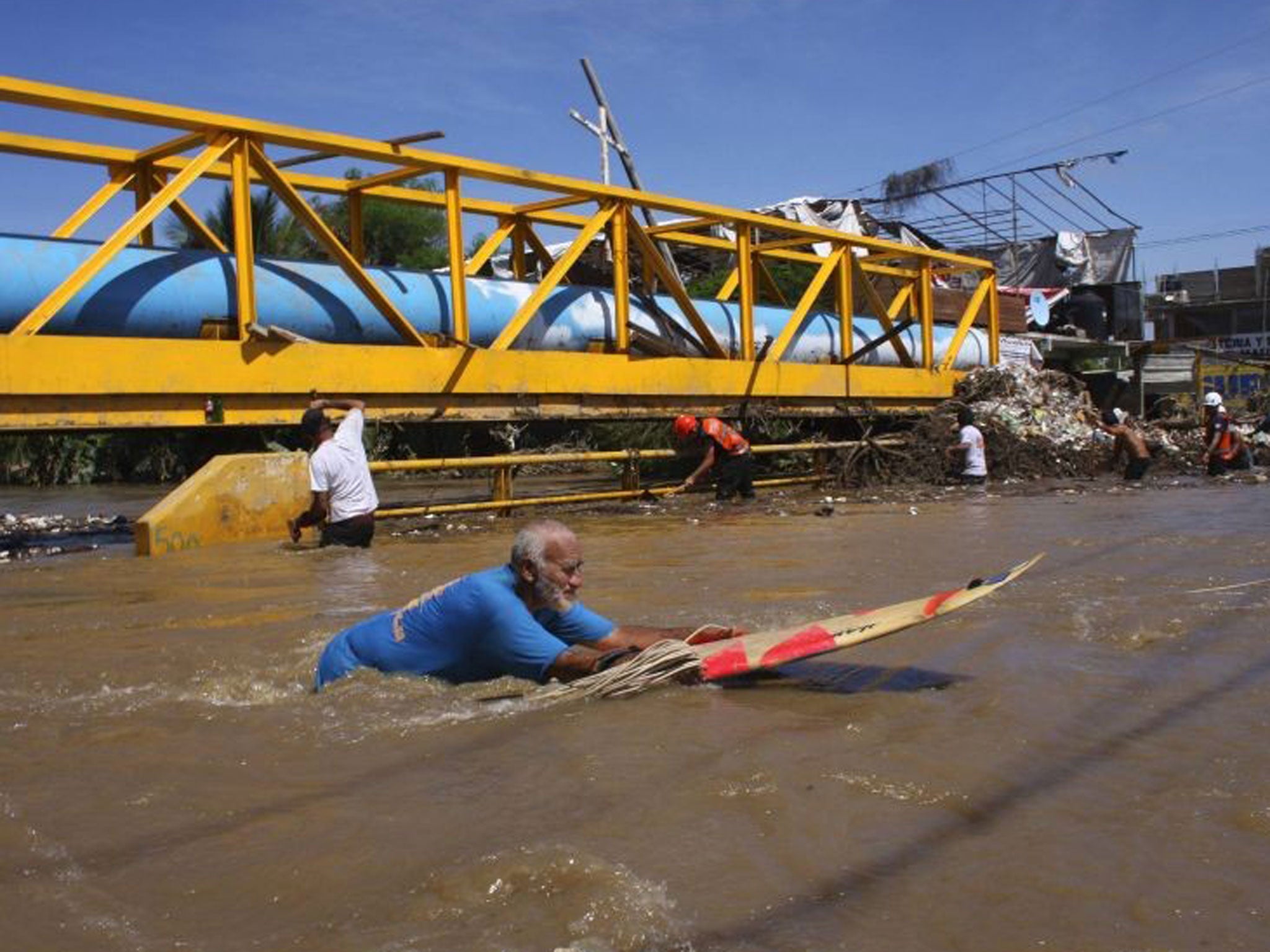A man uses a surfboard to cross a flooded street in Acapulco