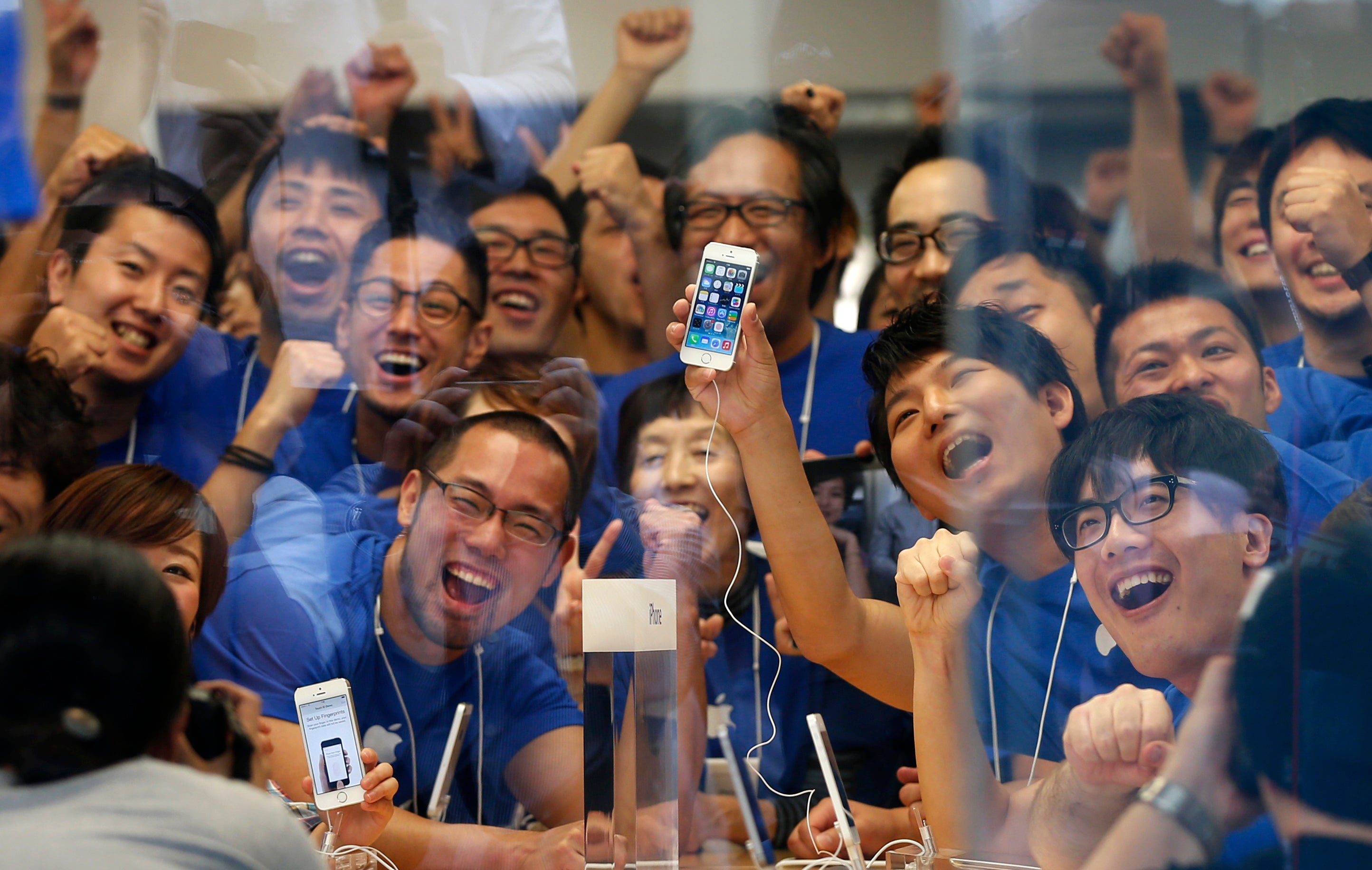 Apple store staff pose with the new Apple iPhone 5S before its goes on sale at an Apple Store at Tokyo's Ginza shopping district September 20, 2013. Picture taken through the shop's window