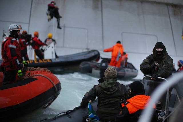 A Russian Coast Guard officer points a gun at a Greenpeace activist as others attempt to climb the Prirazlomnaya oil platform