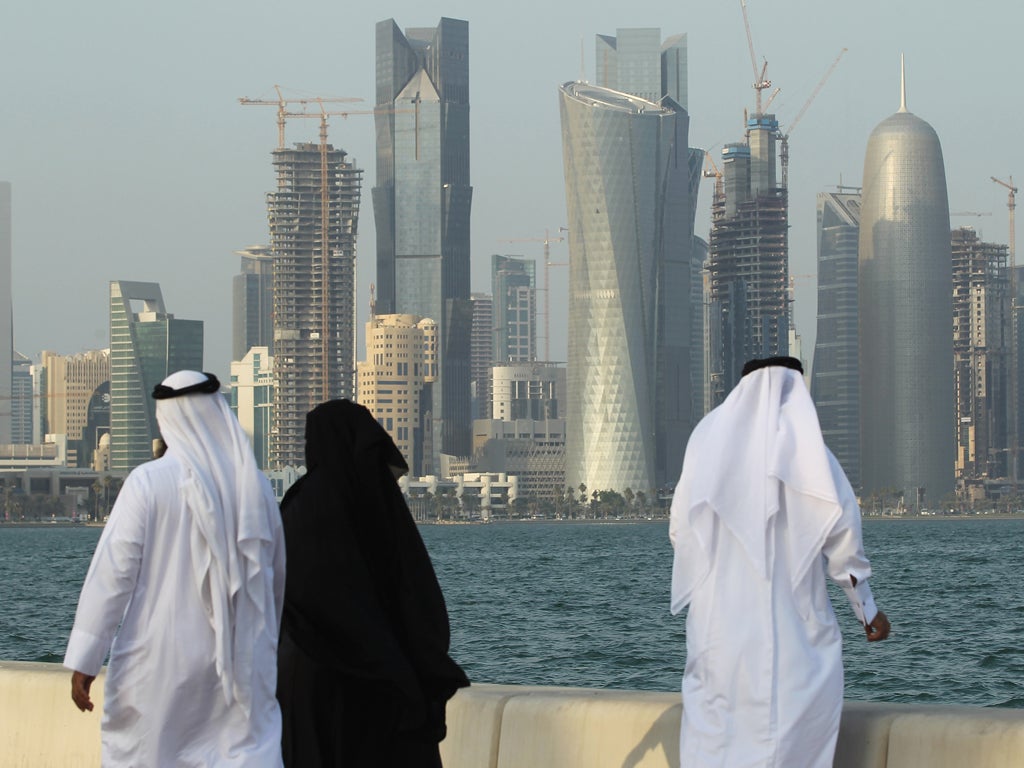 Men and women wearing traditional Qatari clothing visit the waterfront along the Persian Gulf in Doha, Qatar.