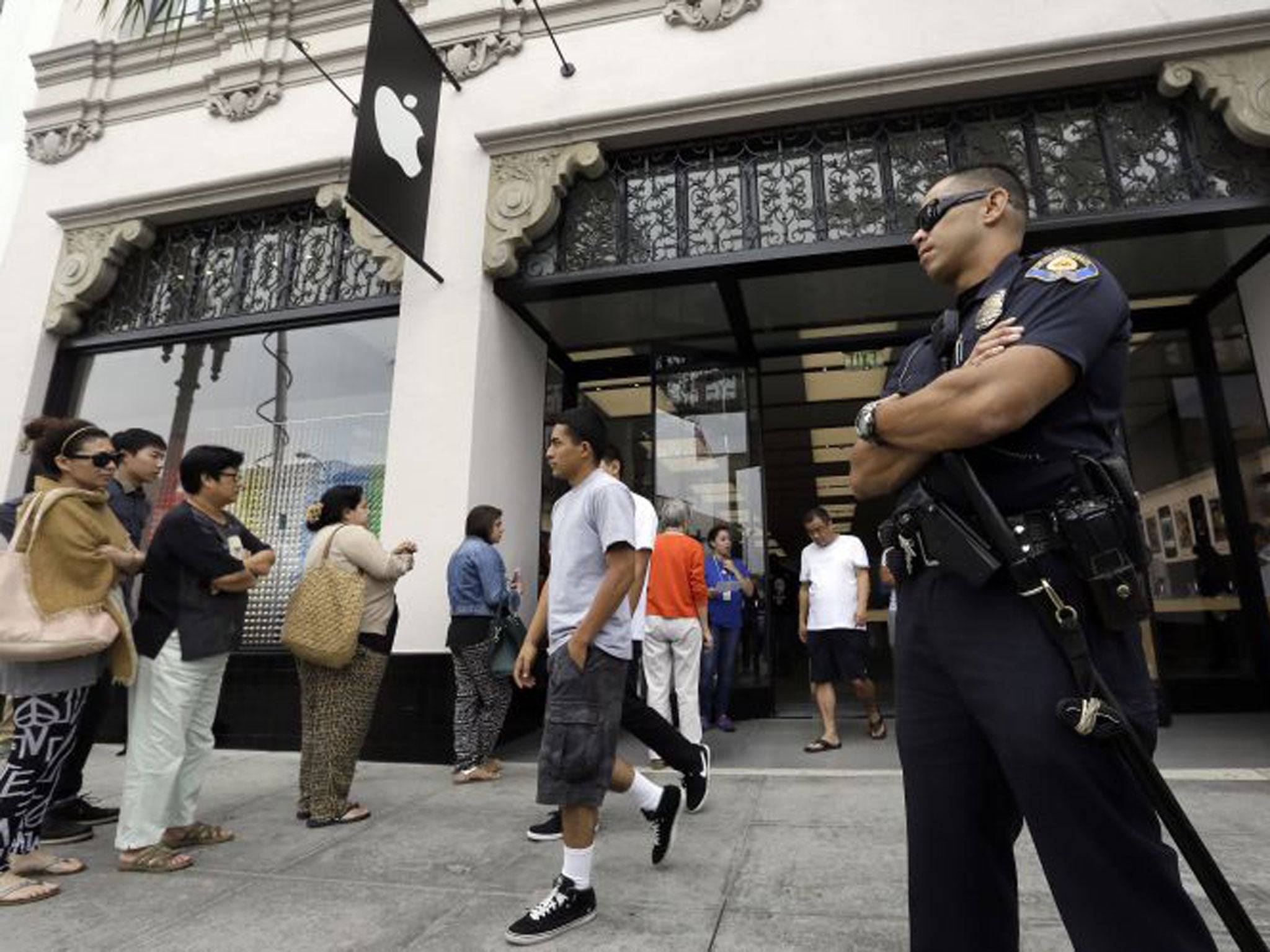 A police officer guards the entrance of the Apple store as customers wait in line for the latest versions of the iPhone during the opening day of sales of the iPhone 5s and iPhone 5C in Pasadena, California