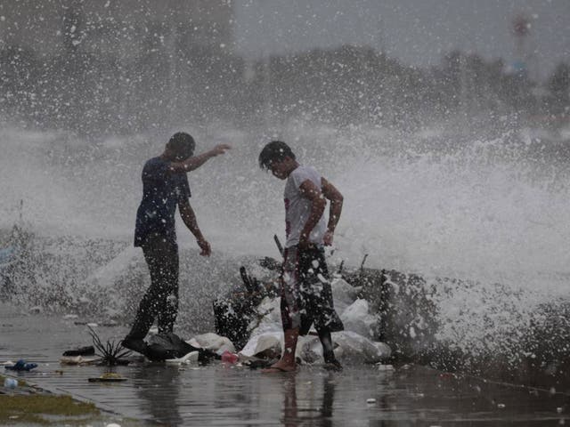 Filipino workers are hit by splashes from a strong wave as it strikes the wall along a bayside promenade in Manila