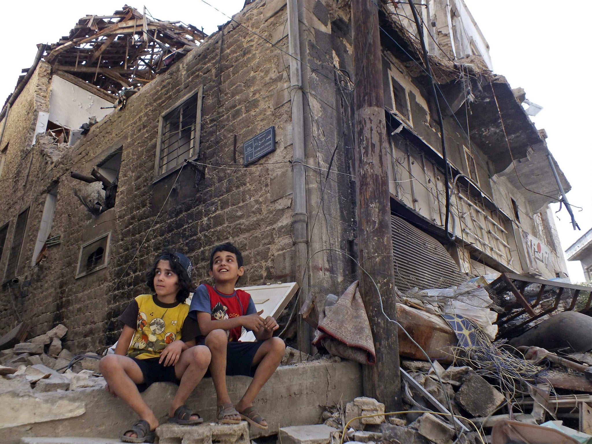 Children sit along a damaged street filled with debris in the besieged area of Homs (Getty)