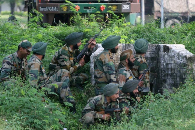 Indian army soldiers gather behind a small wall during an attack by militants on an army camp at Mesar, Samba