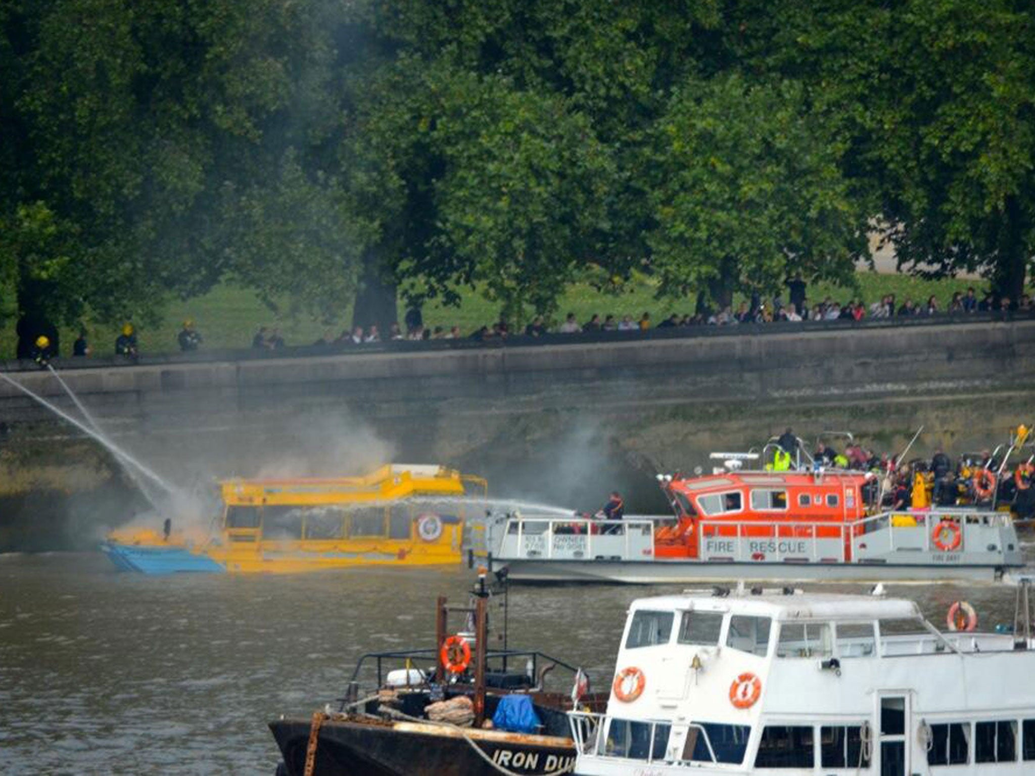 The London Duck Tours boat, left, as rescue services extinguish the flames after it caught on fire near to the houses of Parliament