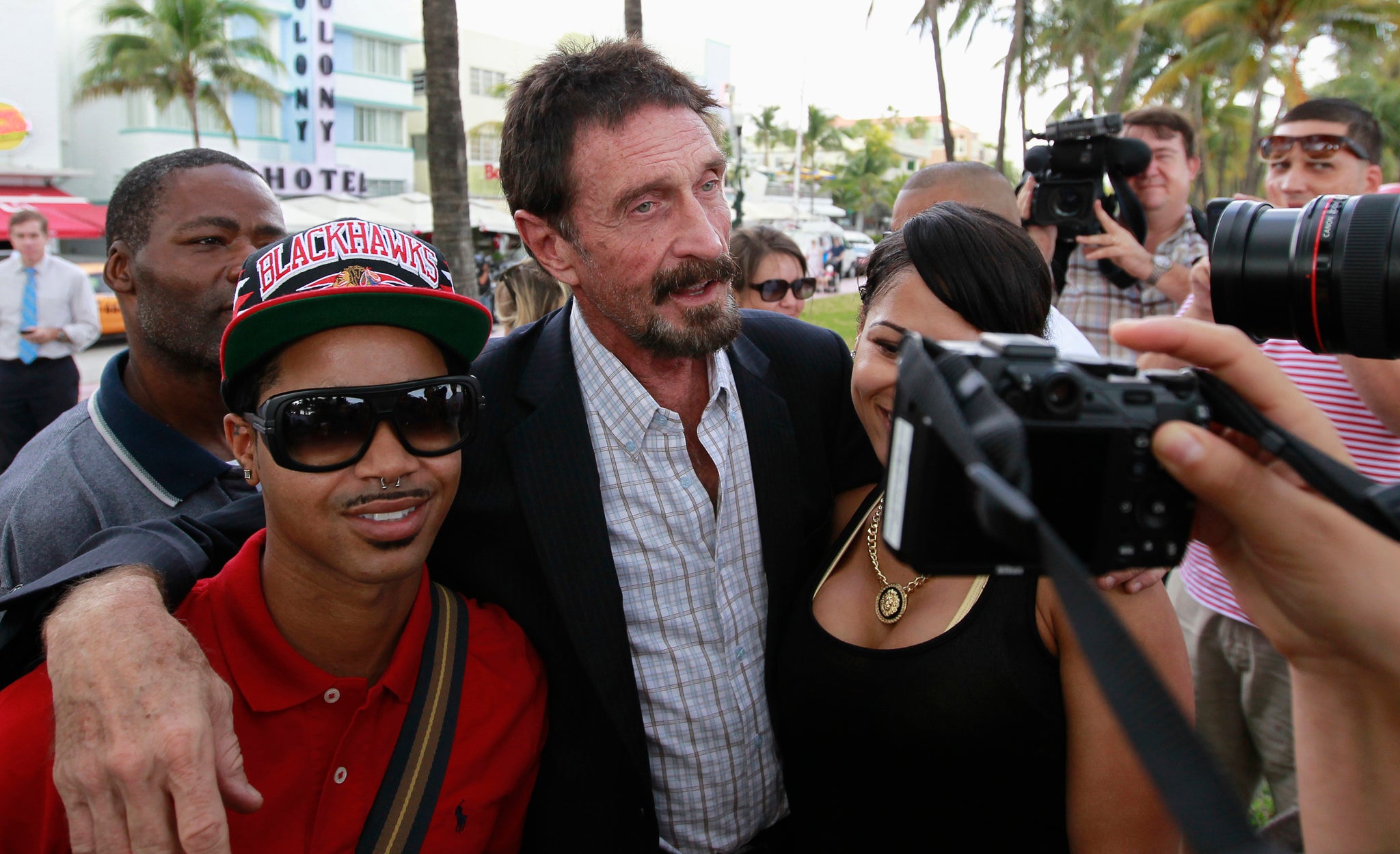 Computer software pioneer John McAfee (C) poses with tourists as he speaks with reporters outside his hotel in Miami Beach, Florida December 13, 2012.