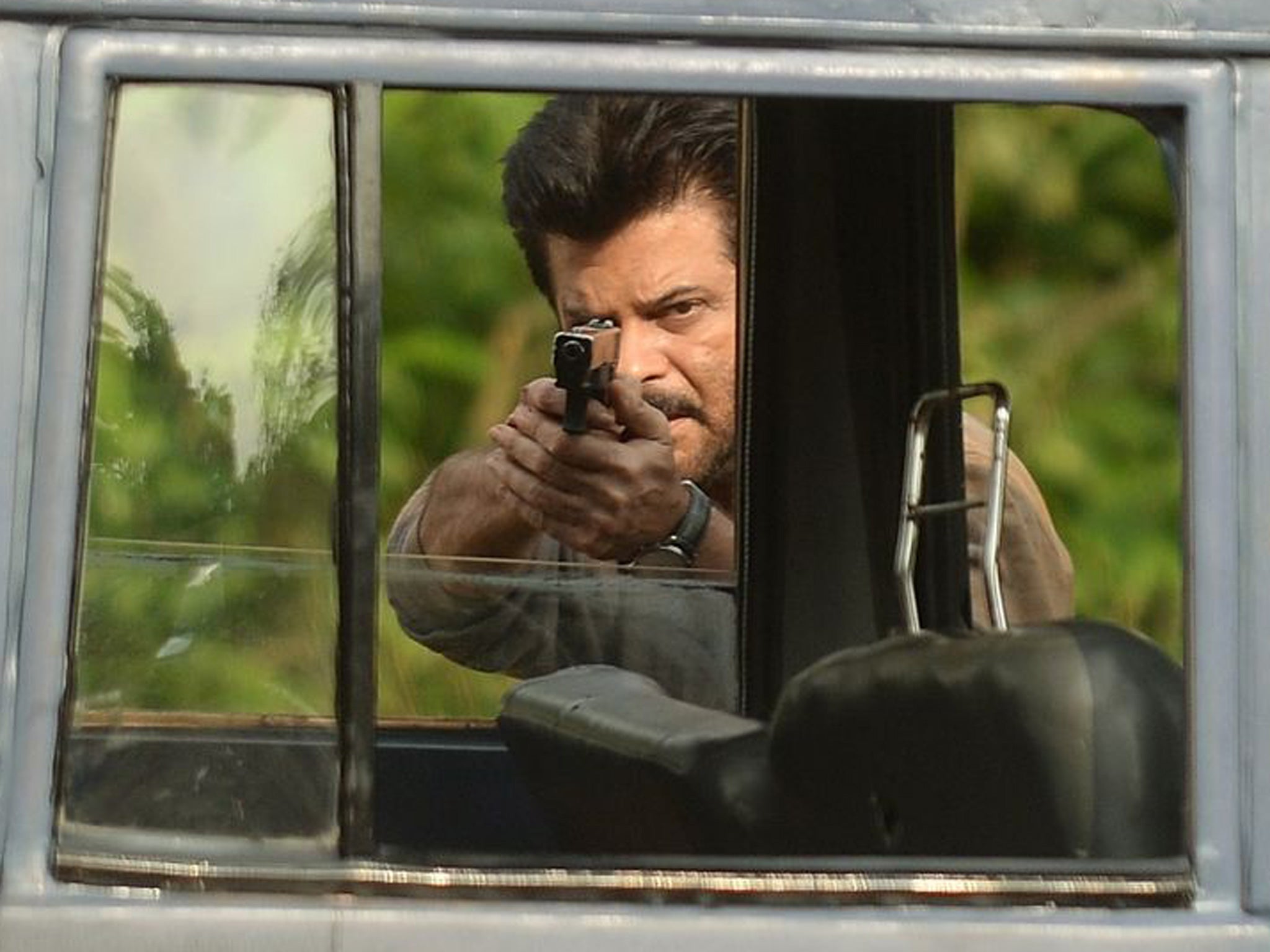 Indian Bollywood actor Anil Kapoor points a gun during shooting for the new television show '24' on location on a film set in Mumbai