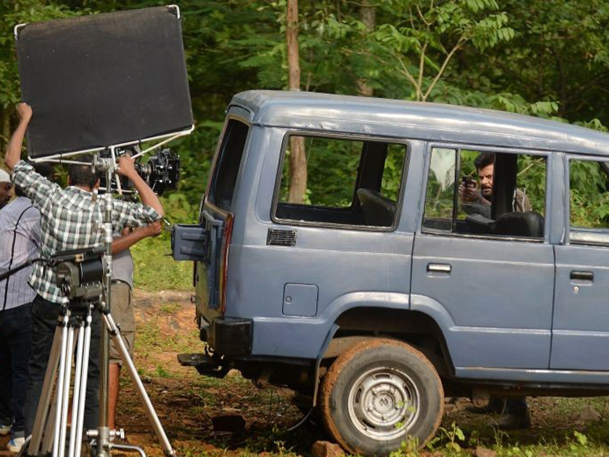 Indian Bollywood actor Anil Kapoor (behind vehicle) points a gun during shooting for the new television show '24' on location on a film set in Mumbai