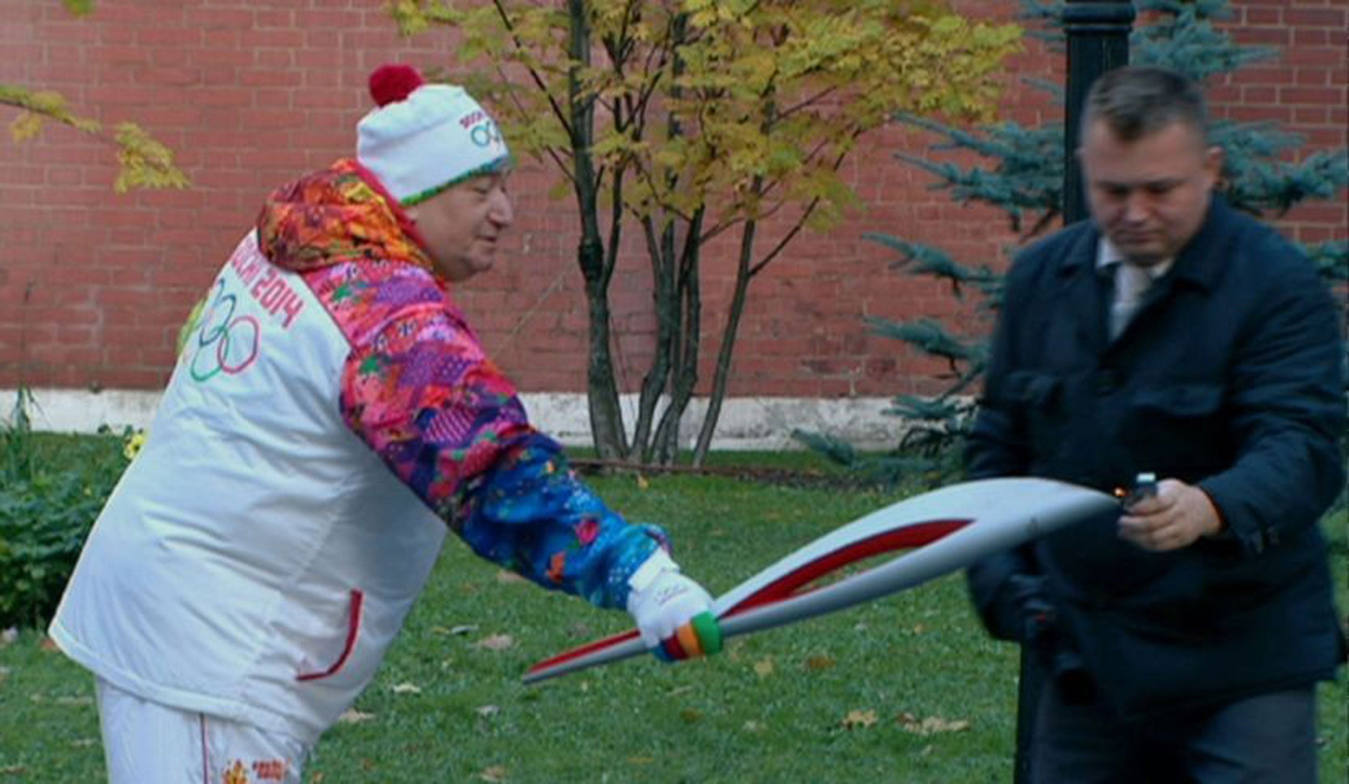 In this frame grab provided by APTN, a security officer lights an Olympic torch for former swimming champion Savarsh Karapetyan after the flame was blown out