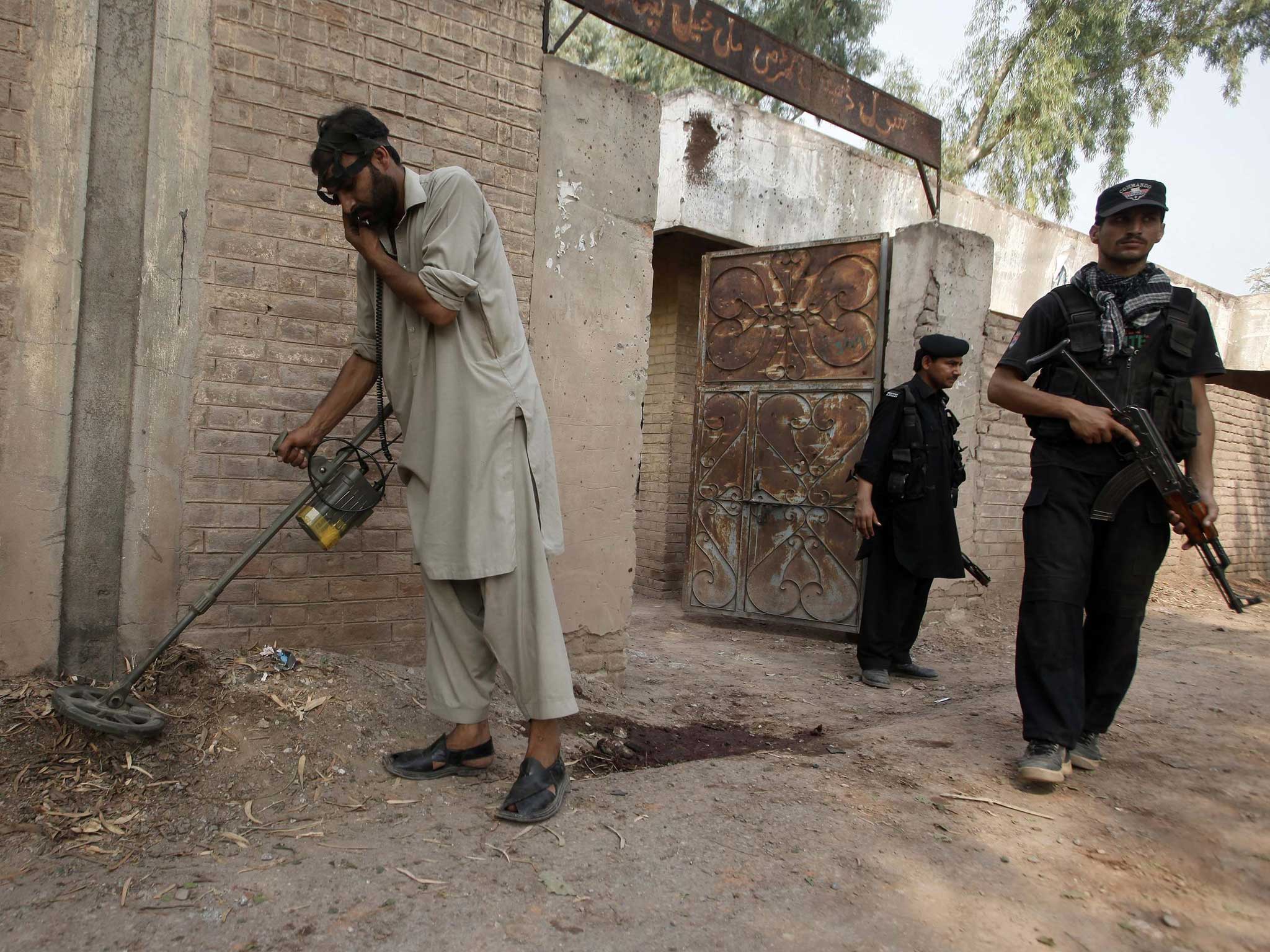 A security official uses a metal detector to survey the site of the bomb blast on the outskirts of Peshawar