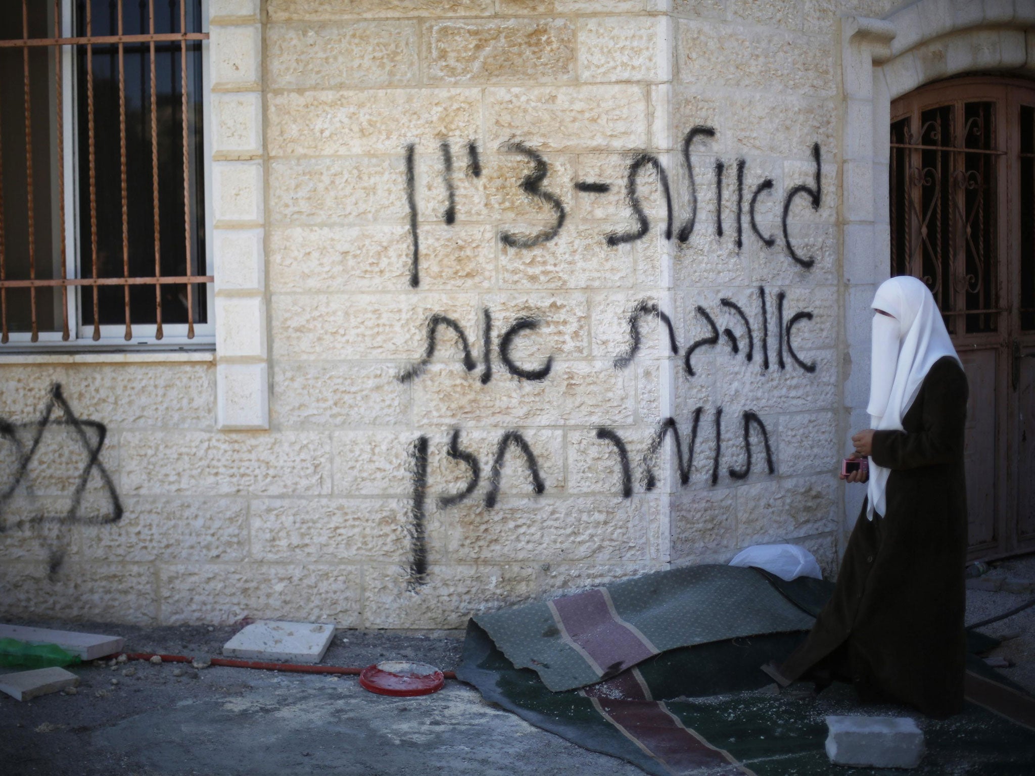 A Palestinian woman walks near the vandalised wall of a mosque in the West Bank village of Burka