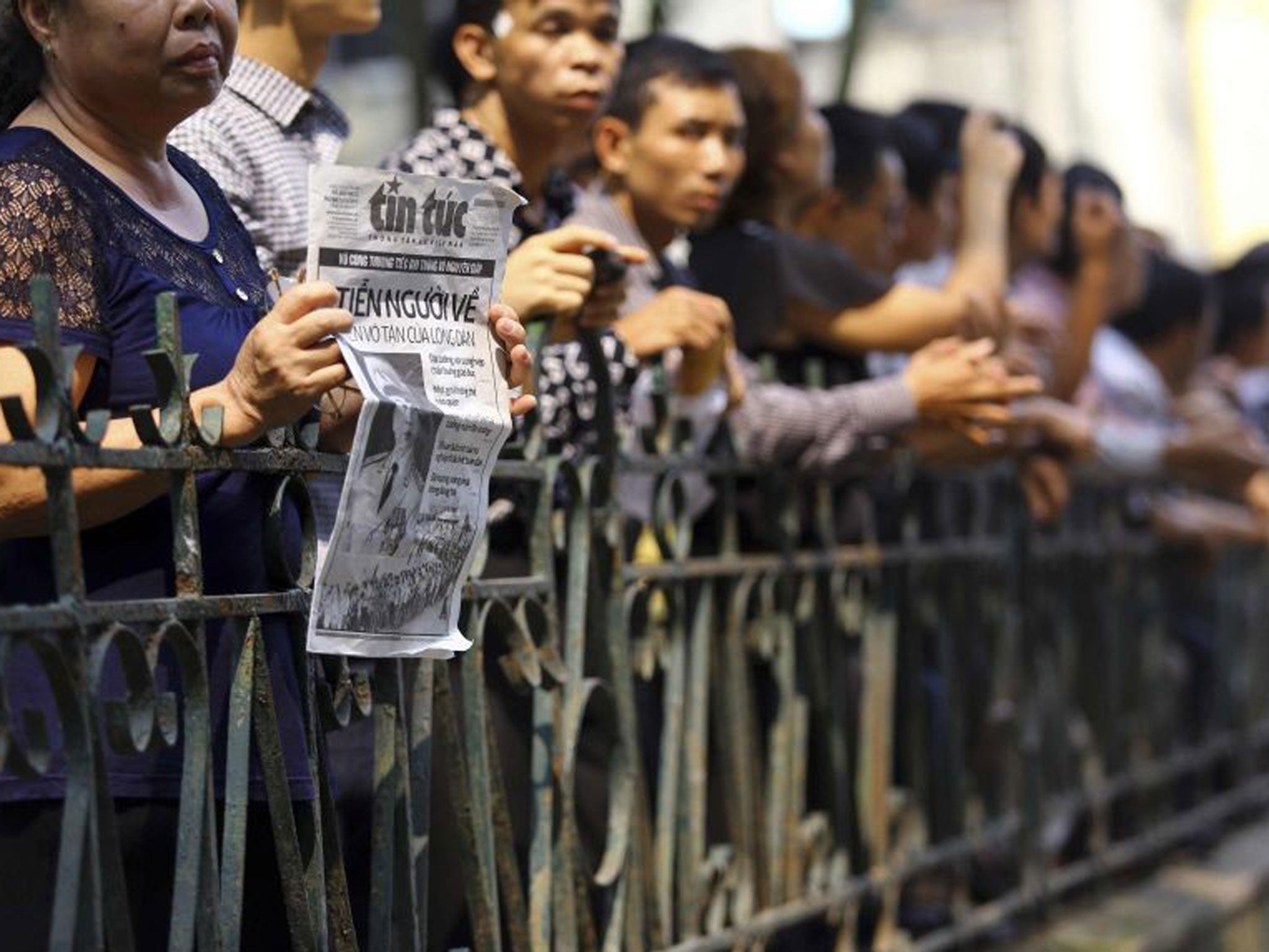A woman holds a newspaper clipping of the late general Vo Nguyen Giap as she stands with other mourners outside the National Funeral House in Hanoi 12 October, 2013