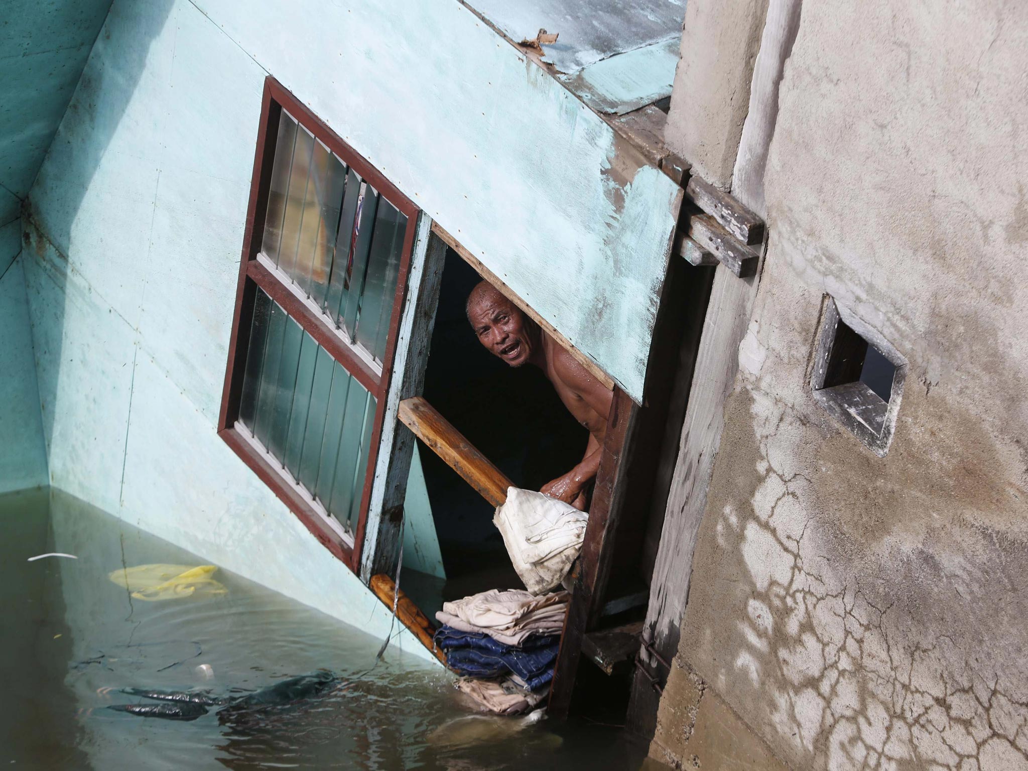 16 October 2013: A resident looks out from a window of his family's home, which fell into a river, after an earthquake in Buenavista, Bohol a day after an earthquake hit central Philippines
