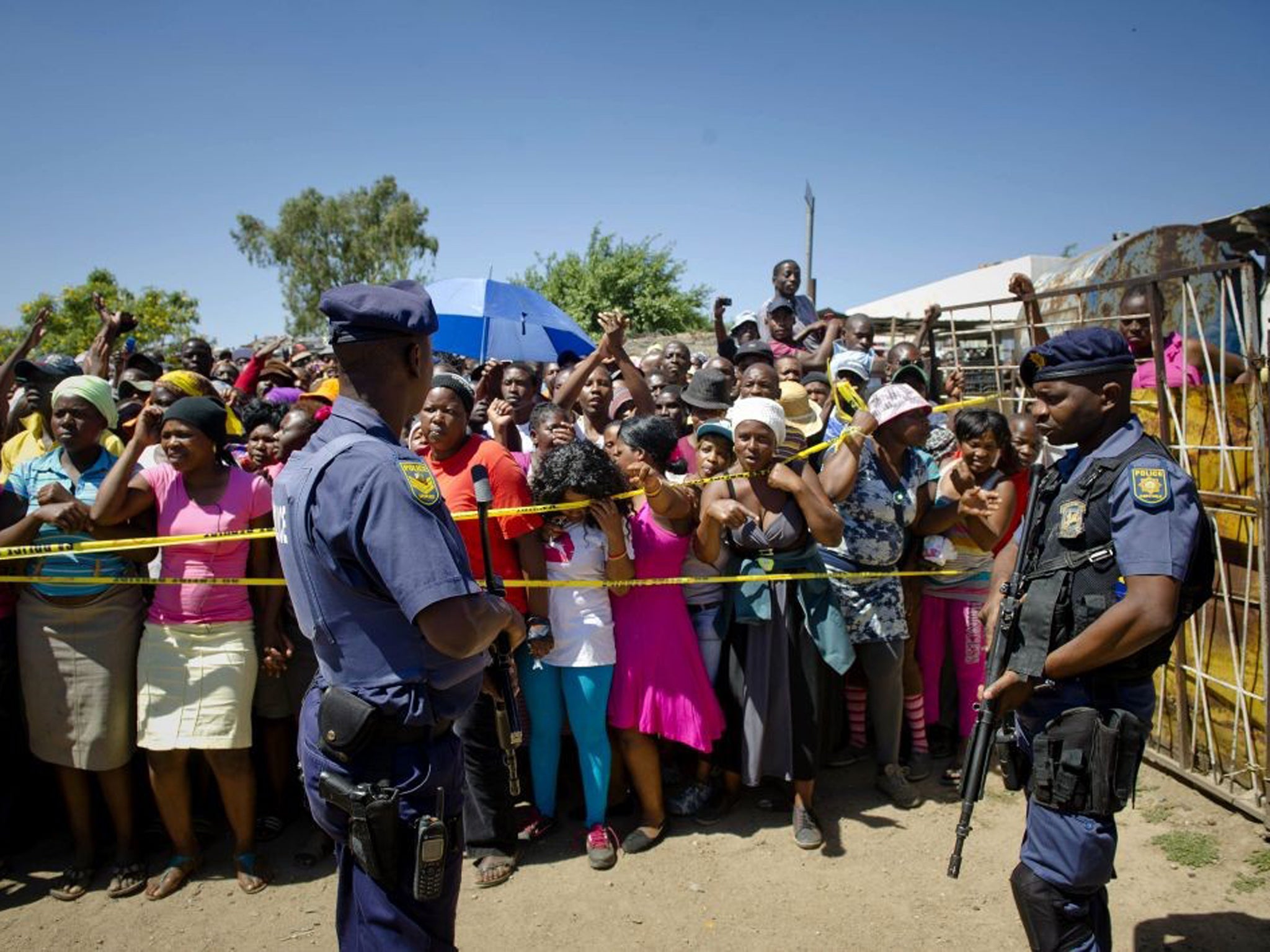 South African police stand guard as residents of Diepsloot township gather outside the crime scene